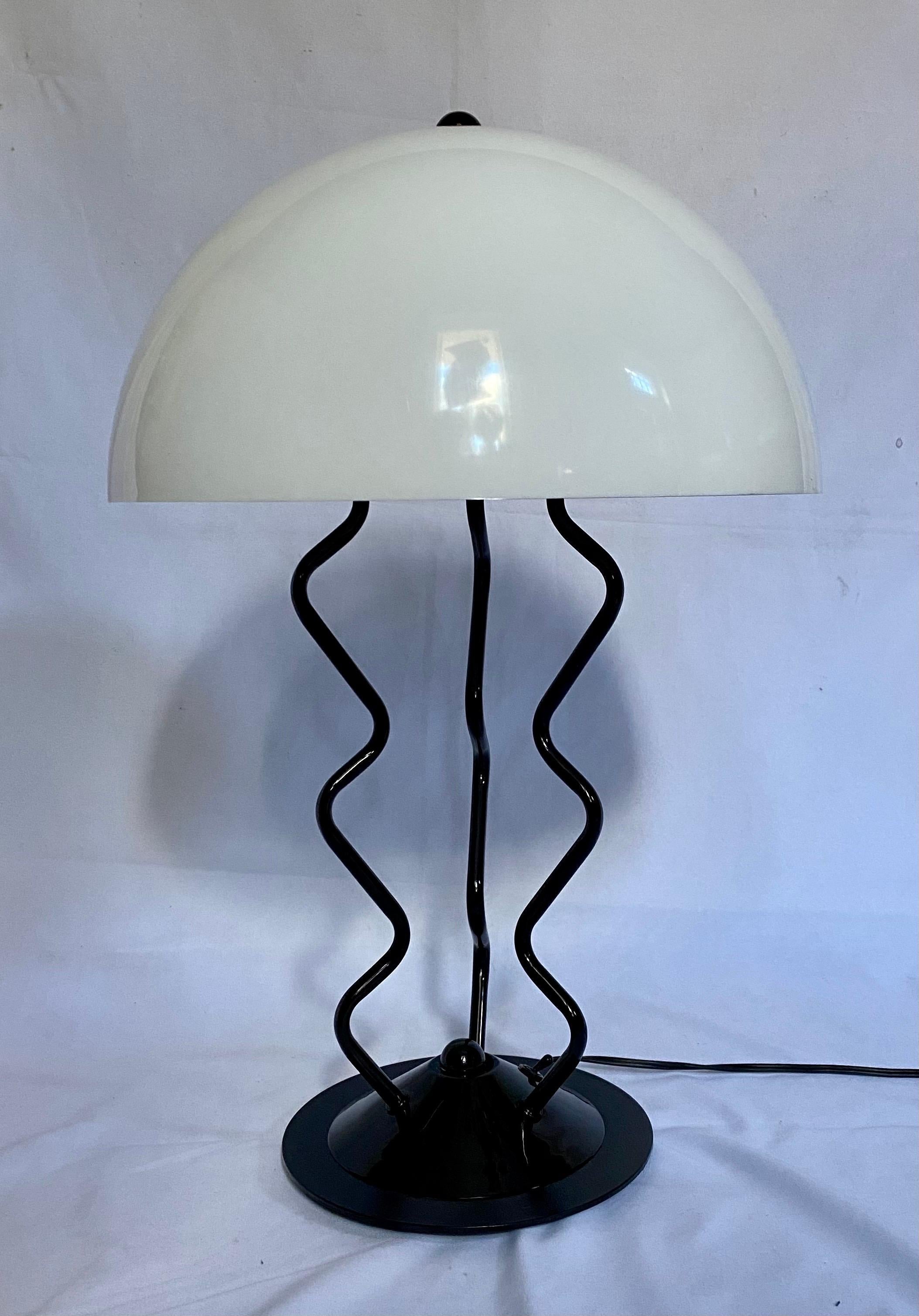 Modern Memphis style table lamp featuring a zig zag gloss black metal base and a white plastic dome shade. Porcelain socket holds a single standard base bulb.