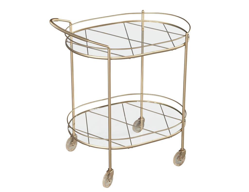 Metal Bar Cart with 2 Tier Glass. Sleek modern metal frame in a beautiful satin champagne color tone. Unique spun metal handle and acrylic wheels elevate the design. Completed with 2 tier glass shelves supported by metal criss-cross supports.