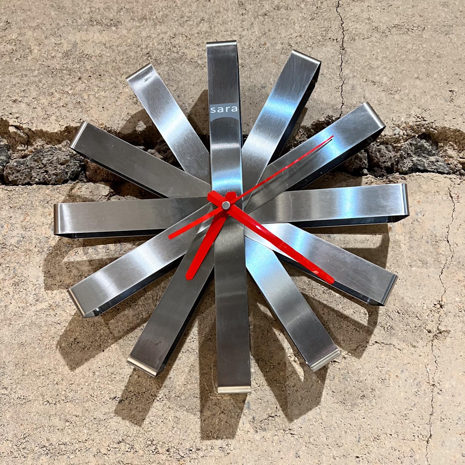 Sara Ribbon Metal Wall Clock 
stainless steel
2 d x 12 diameter
Preowned vintage condition
See all images for condition.