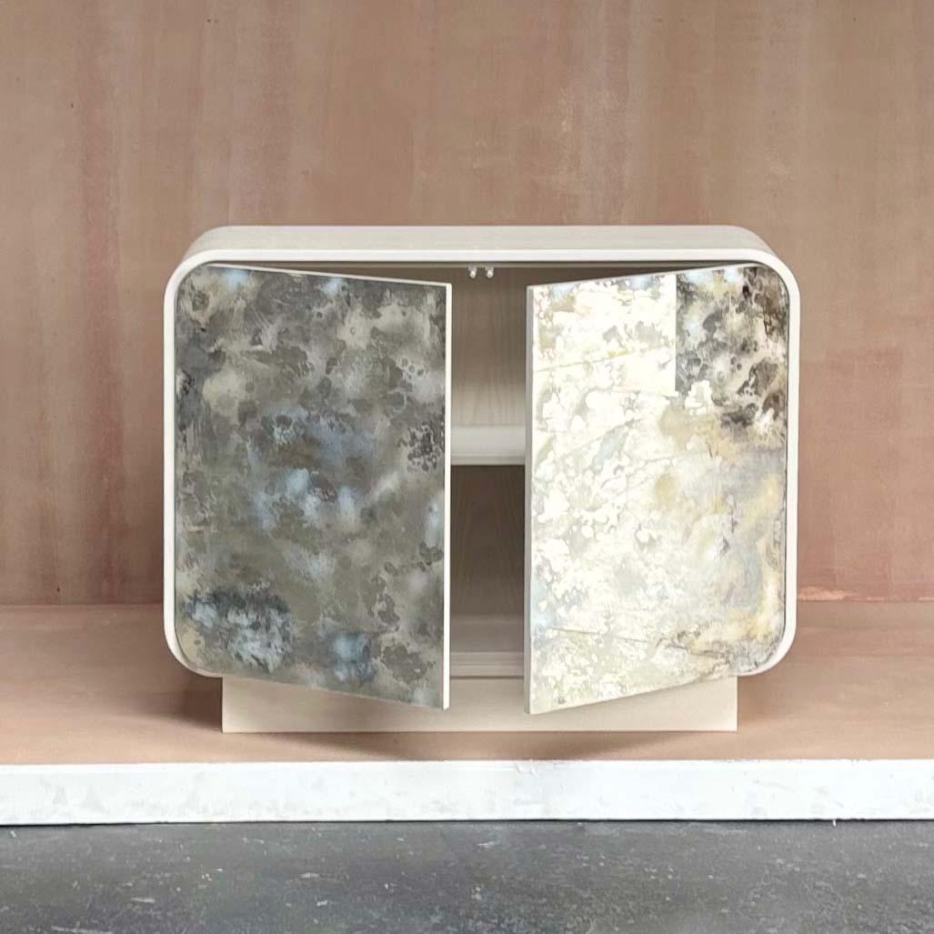 Il buffet moderno Mezza Luna Curved Two Door White Dust Eglomise Platform di Ercol è caratterizzato da una silhouette curva con finitura Sand on Oak. Le due porte con chiusura a sfioramento sono caratterizzate da pannelli di polvere bianca eglomise