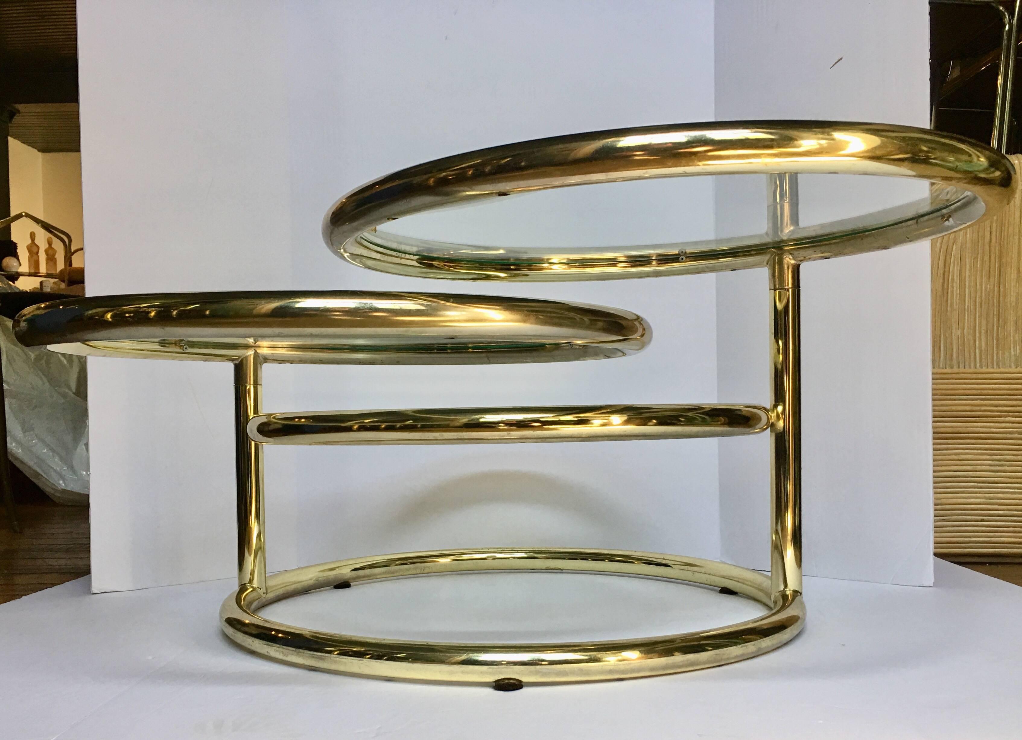 Modern three-tier brass plated swivel cocktail table featuring a tubular frame with removable clear glass inserts. Top and second tier swivel. Table measures 66 inches long when both tiers are fully extended. Third tier is stationary.  In the style