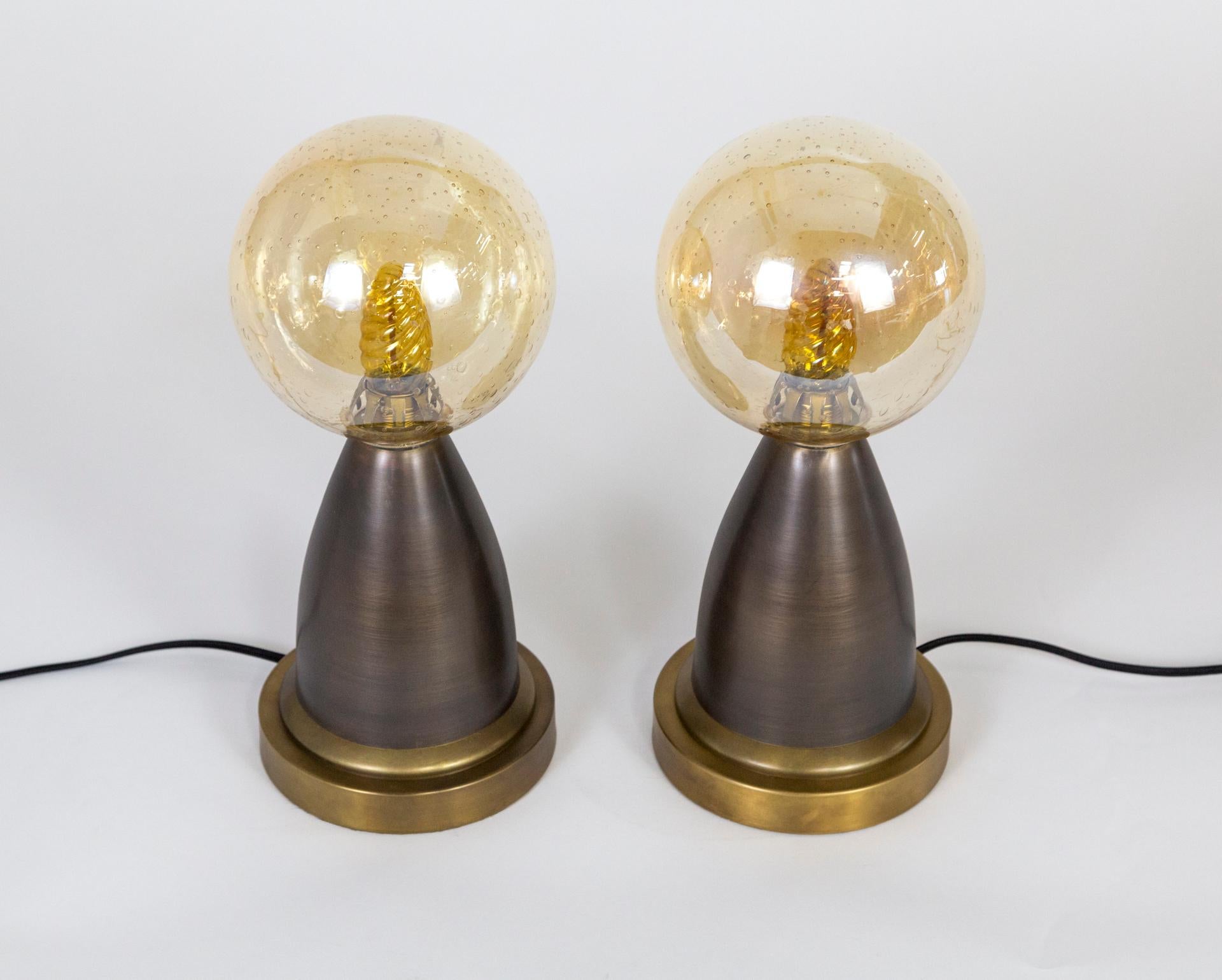 Modern and Minimalist; this petite brass pair of table lamps feature amber seeded glass globes. Each has a felted bottom, on/off switch on the cord and one E12 candelabra socket. Measures: 13.5