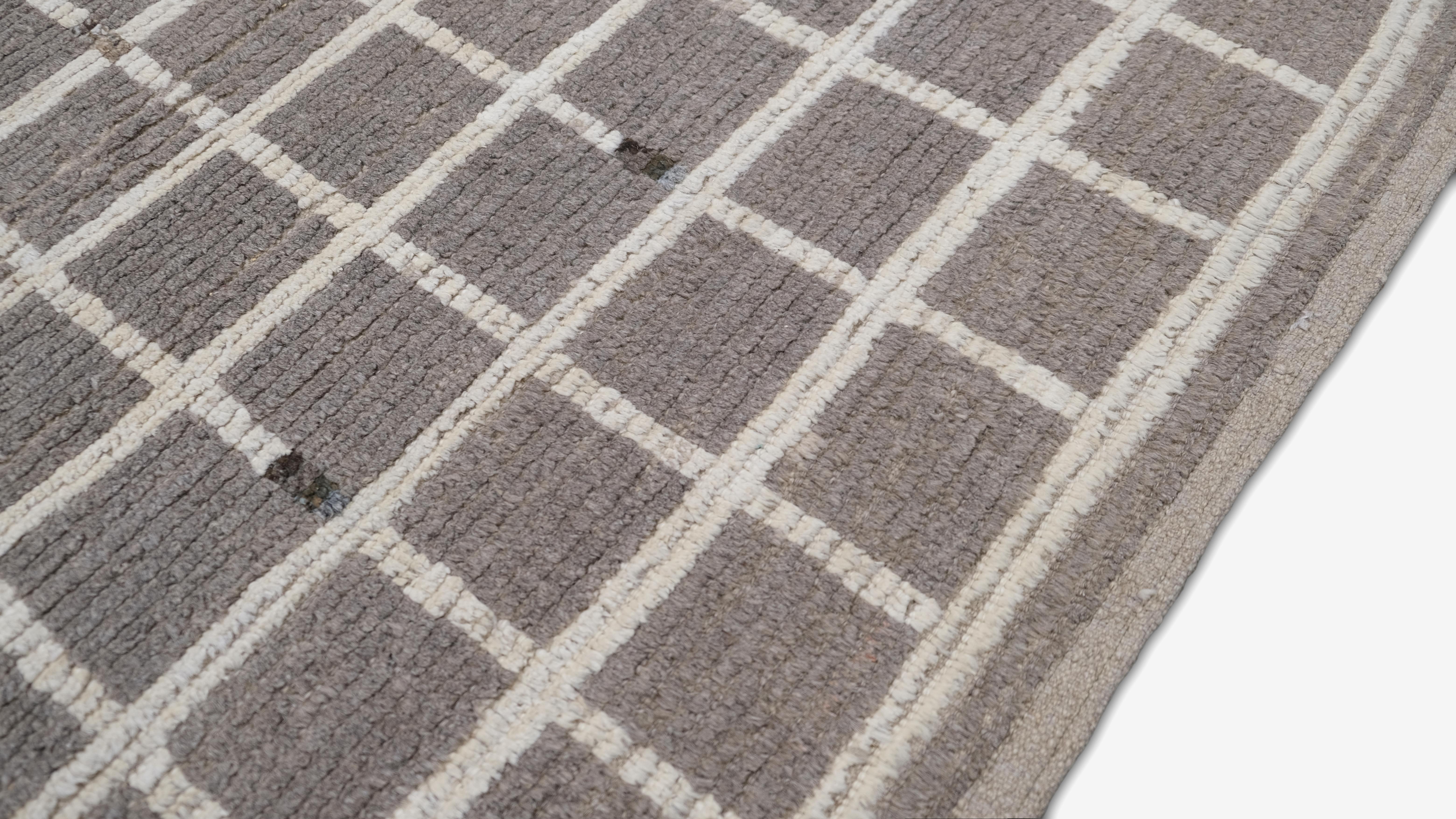 Dieser handgeknüpfte Wollteppich zeichnet sich durch ein auffälliges modernes Gittermuster aus, das zeitgenössisches Design mit handwerklicher Kunstfertigkeit verbindet. Die neutrale graue und elfenbeinfarbene Palette schafft ein vielseitiges