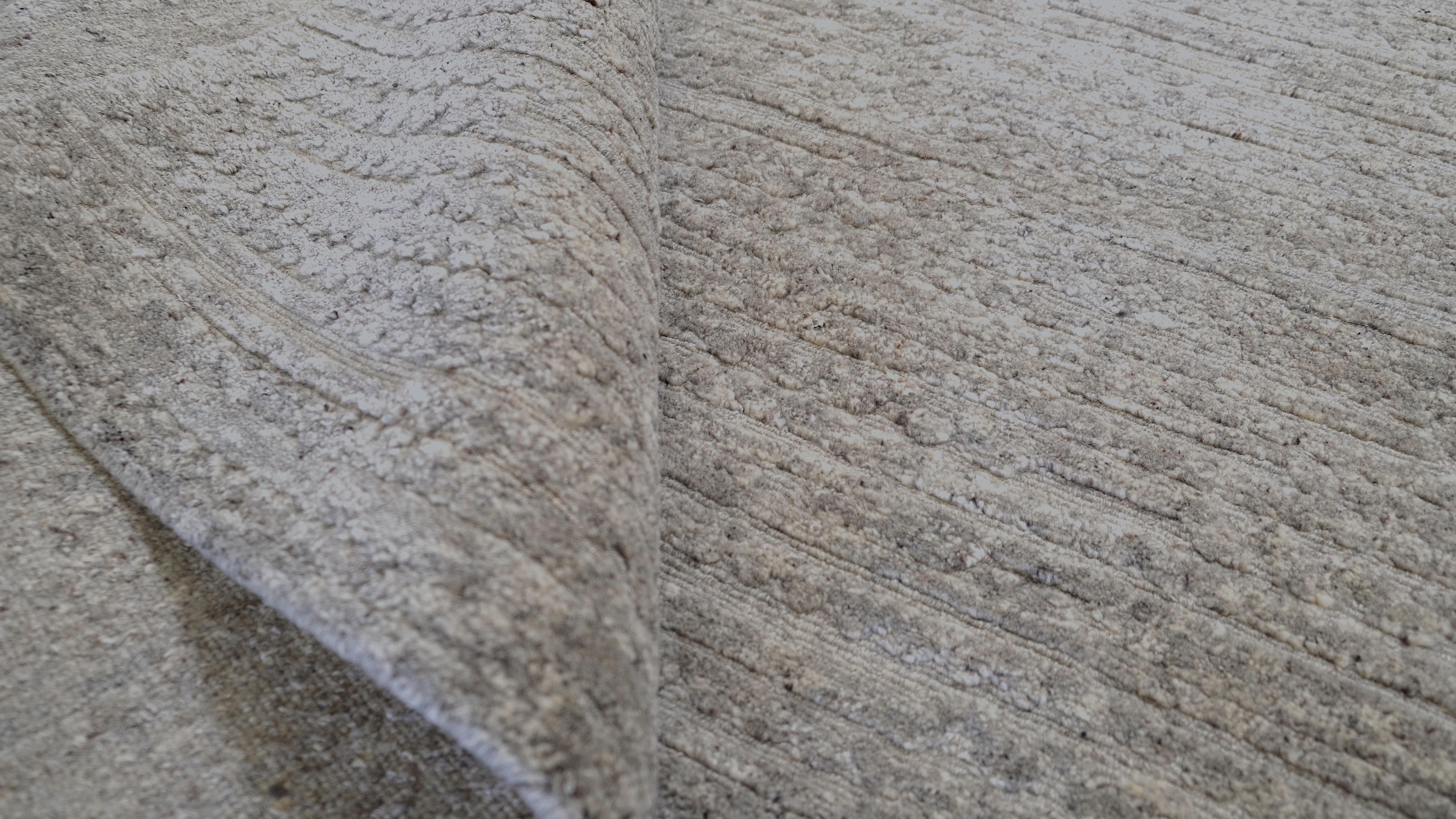 Dieser handgeknüpfte Wollteppich verkörpert mit seinem dezenten, neutralen Taupe-Ton und seiner raffinierten Textur schlichte Eleganz. Der aus hochwertiger Wolle gefertigte Teppich zeichnet sich durch eine moderne, minimalistische Ästhetik aus, die