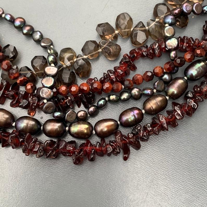 Questa splendida collana a torciglione è un capolavoro moderno, con un design fatto a mano in argento sterling e una splendida combinazione di pietre vere e perle d'acqua dolce. La collana presenta perle di granato, perle a goccia di topazio fumé