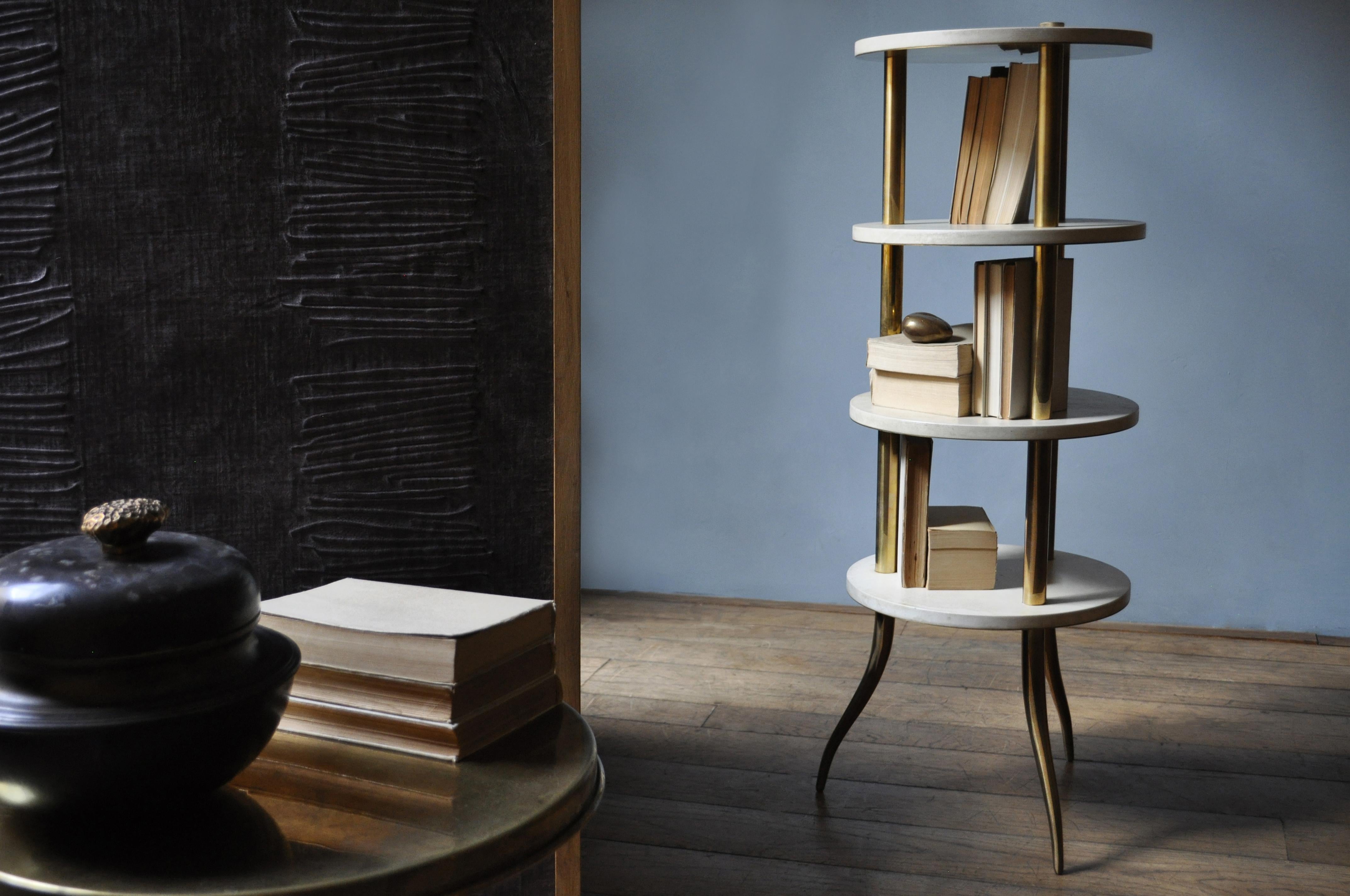 Distinguished for its essential shape, freefrom superfluous elements, this column bookcase is characterized by soft colors of parchment leather and shiny brass that give it a retro charm. The structure in brass is made up of three columns with