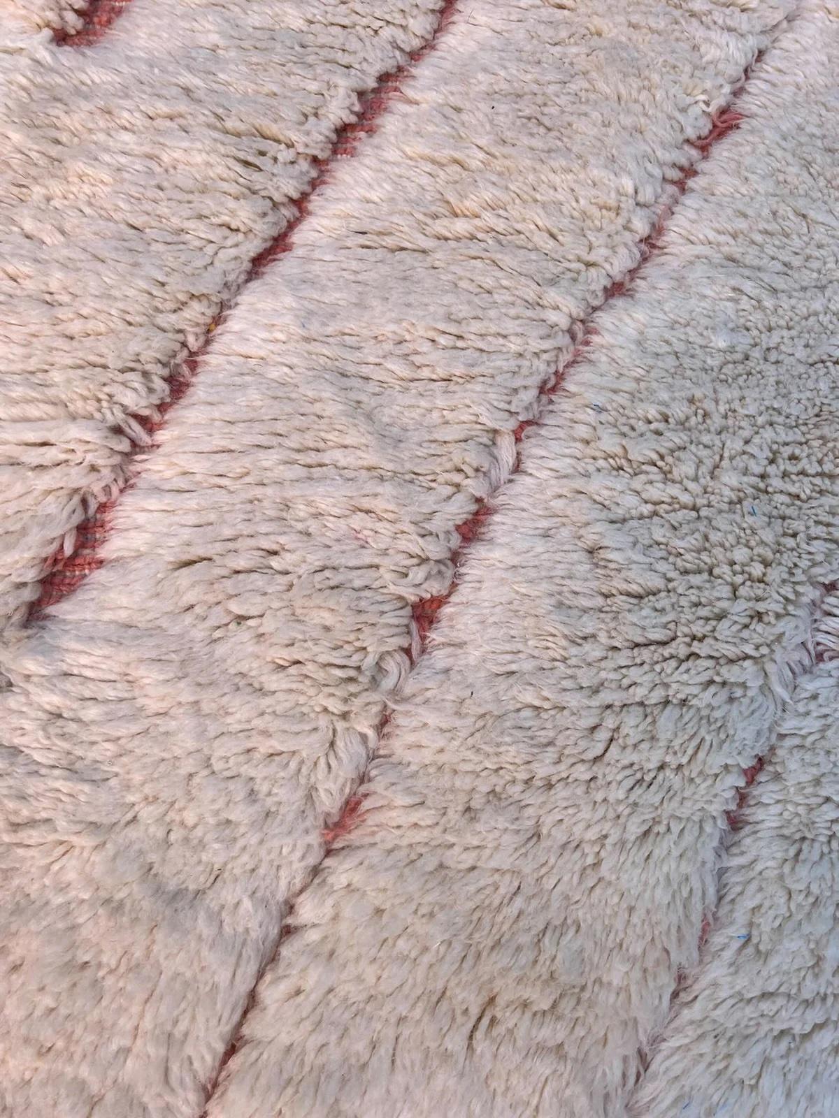 Questo tappeto marocchino di medie dimensioni, color crema, è stato realizzato a mano su un telaio tradizionale da abili artigiani nelle montagne dell'Atlante. È realizzato con lana M'Rirt, ultra lussuosa e di alta qualità. Si tratta di un perfetto