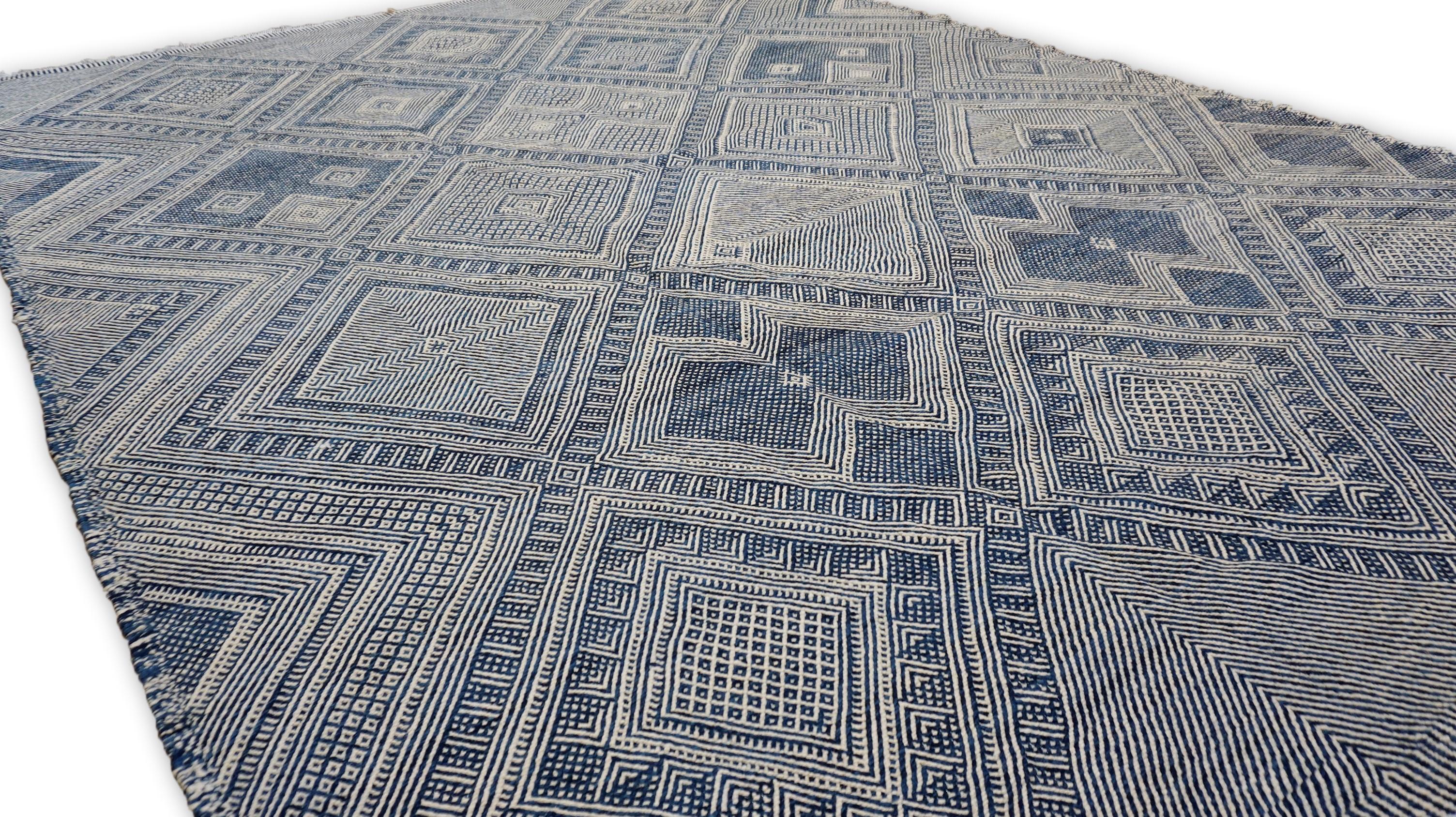 Diese  Der handgeknüpfte Wollteppich zeigt mit seinen kunstvollen Rautenmotiven und fein detaillierten geometrischen Mustern die traditionelle Handwerkskunst der Berber. Der Teppich ist in einer raffinierten Blau- und Elfenbeinfarbe gehalten und