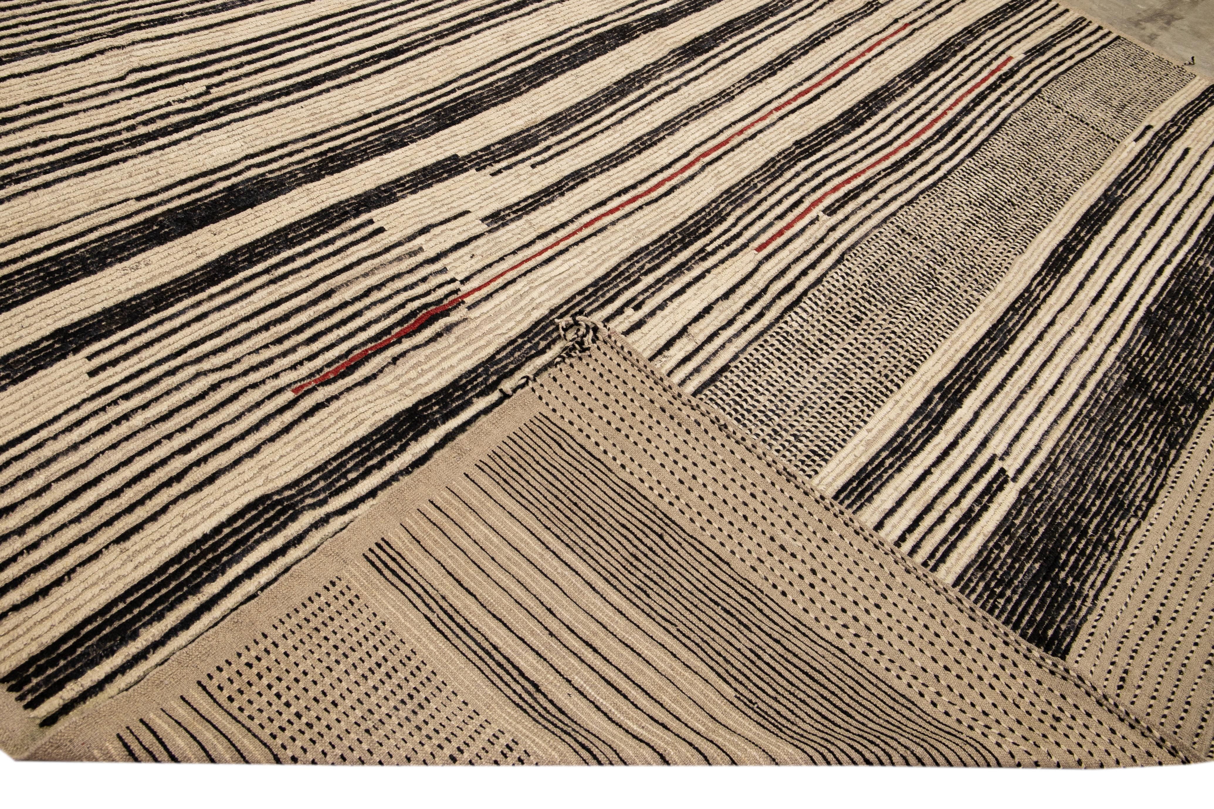 Beautiful Moroccan style handmade wool rug with a beige field. This Modern rug has black accents featuring a gorgeous all-over striped motif.

This rug measures: 12'5