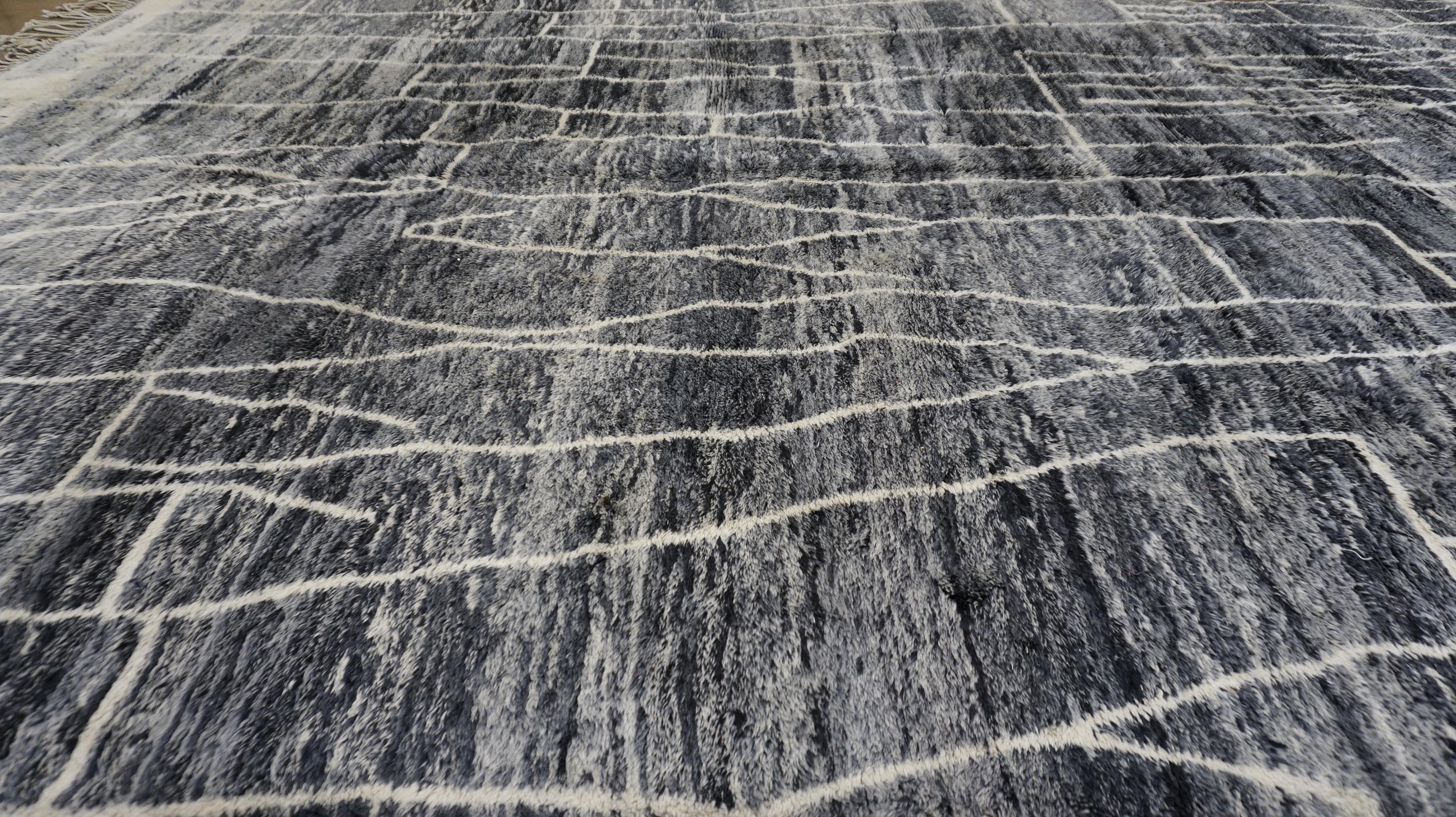 This hand-knotted wool rug showcases a striking modern abstract design inspired by tribal Berber patterns. The charcoal-gray field is enriched with subtle tonal striations that give the rug a dynamic, almost watercolor-like effect. Intricately