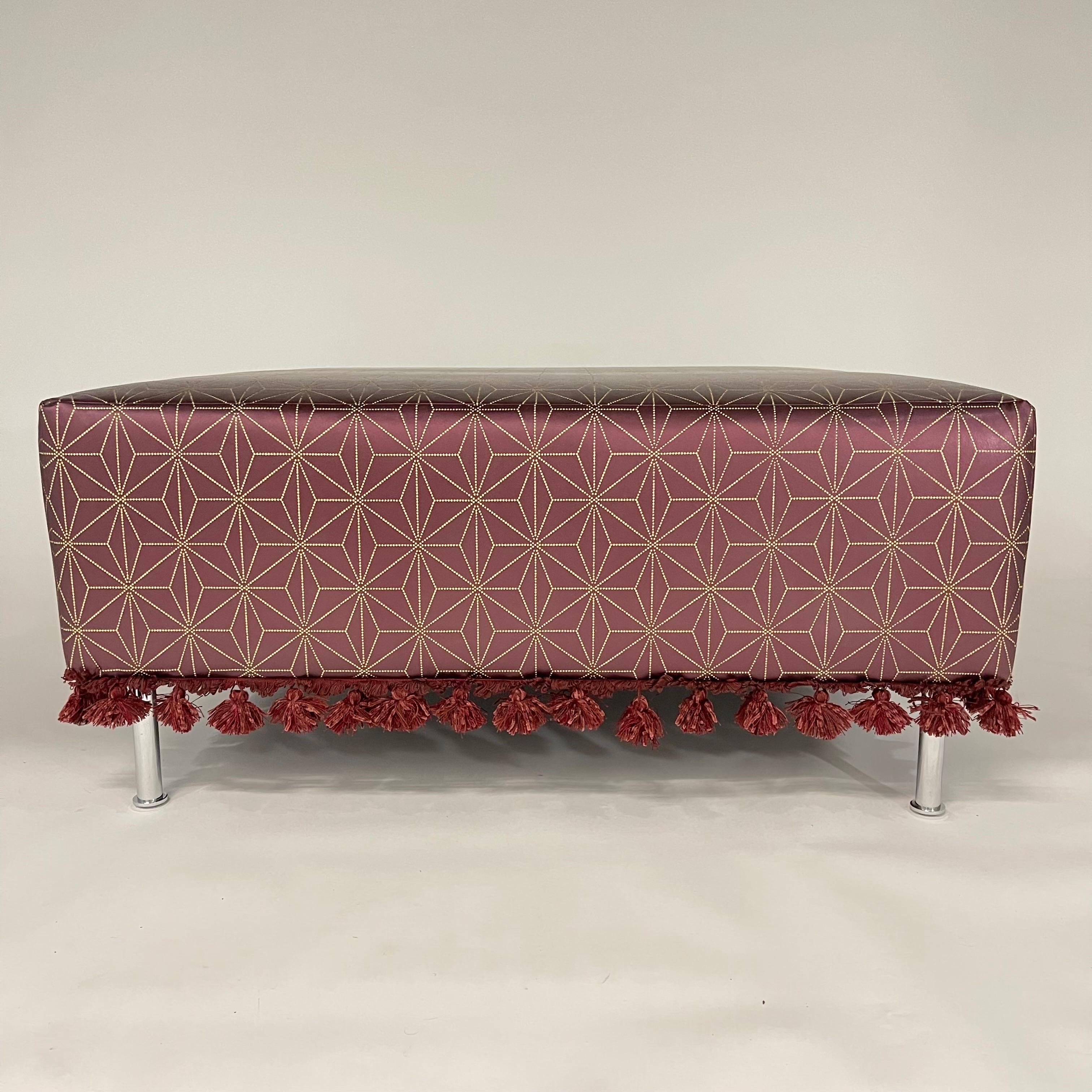Unique Modern Moroccan Ottoman or Foot Stool, rendered in Burgundy Wine colored leather embossed with a moroccan print in gold with a tassel trim detail around the base of 4 polished stainless steel legs.  USA