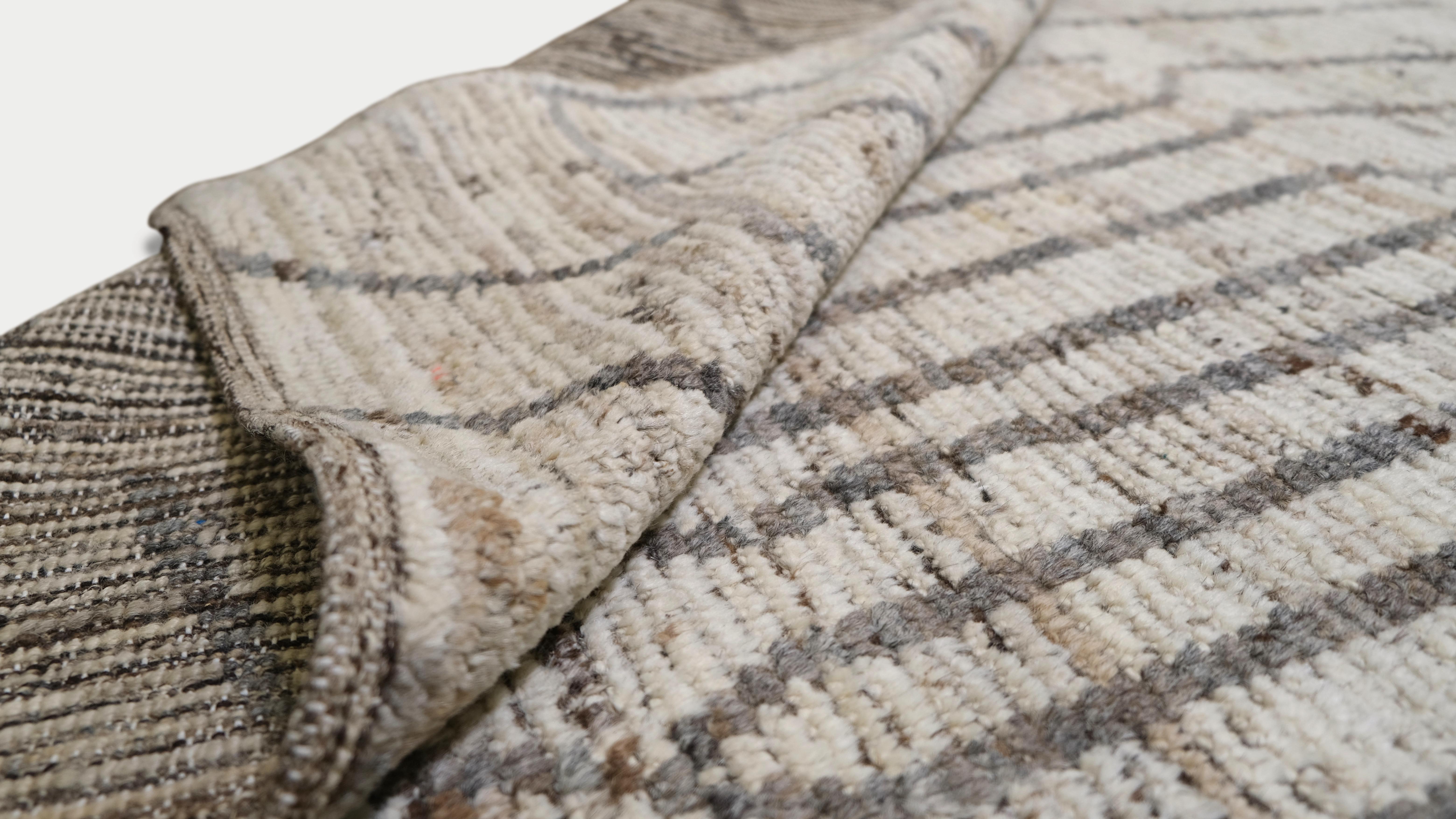 Werten Sie Ihre Einrichtung mit diesem exquisiten, handgeknüpften Wollteppich auf. Dieser Teppich zeigt ein raffiniertes geometrisches Muster in neutralen Elfenbein- und Grautönen und verbindet traditionelle Handwerkskunst mit modernen