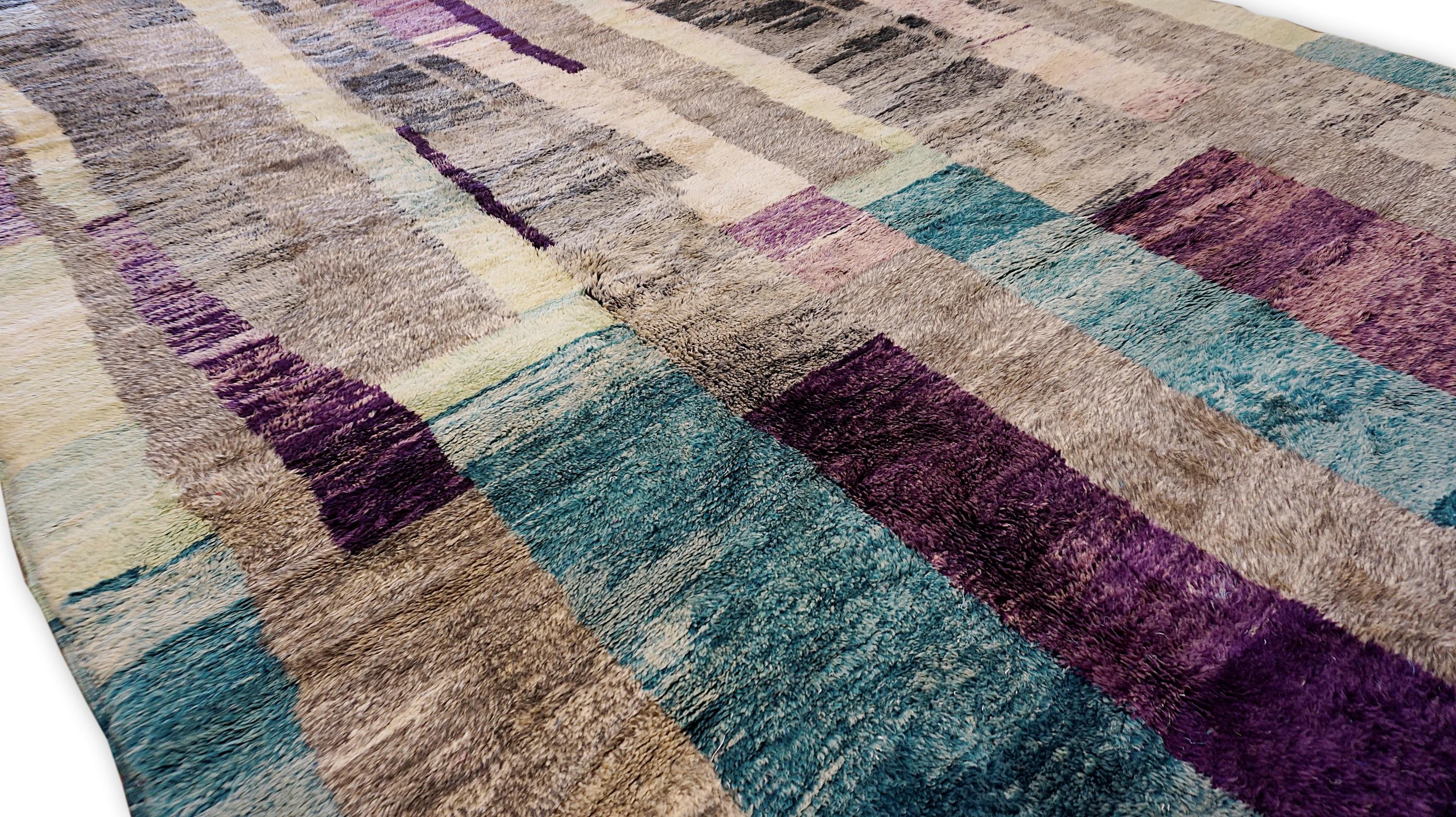 Questo straordinario tappeto in lana annodato a mano è una vibrante espressione di arte tribale che si fonde con un moderno design astratto. Caratterizzato da un'accattivante palette di colori nei toni del viola, del rosa, del grigio e del blu, il