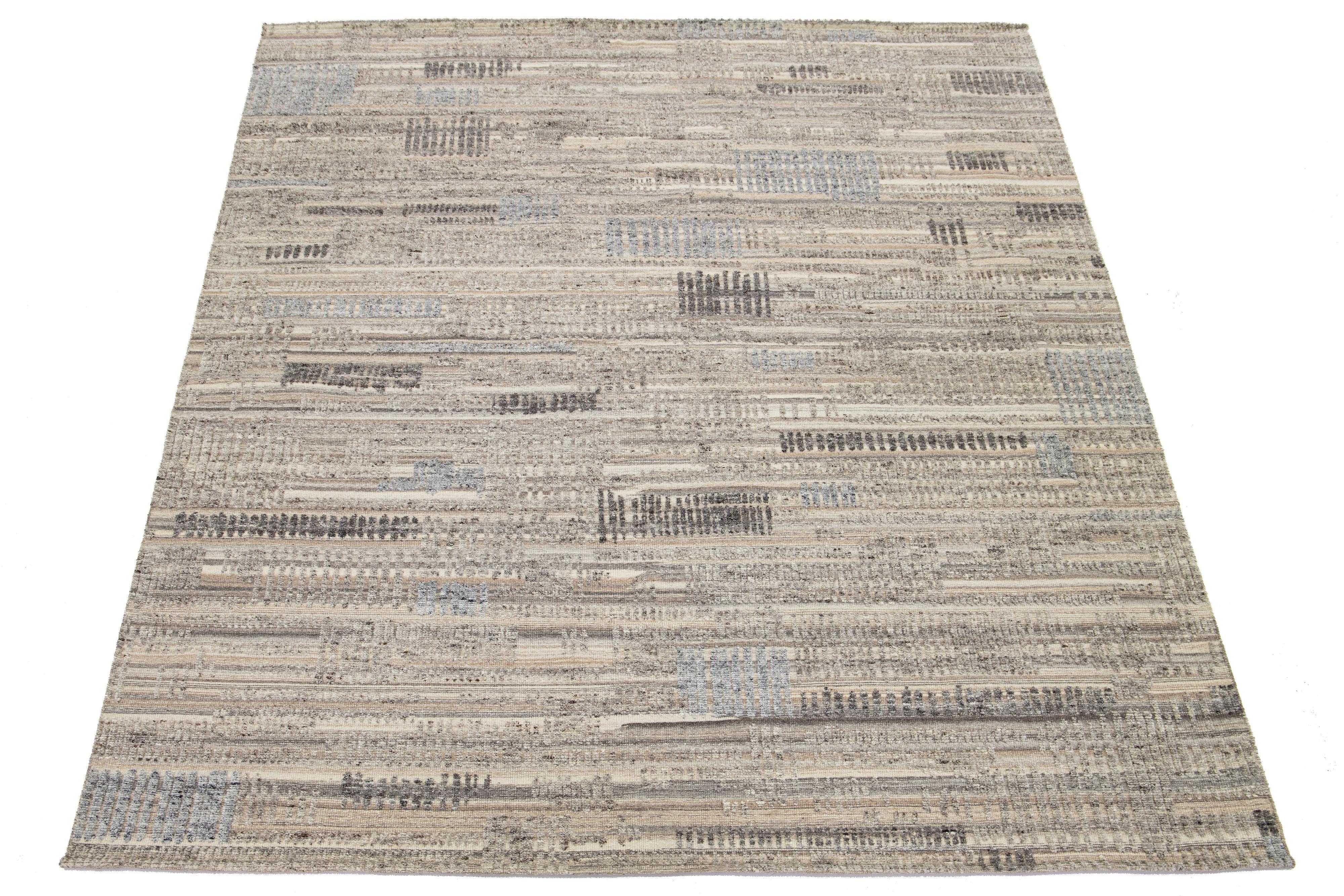 Questo tappeto in lana annodato a mano presenta una lussuosa base beige con un motivo geometrico in marrone chiaro e grigio, ispirato al design marocchino contemporaneo.

Questo tappeto misura 9'1