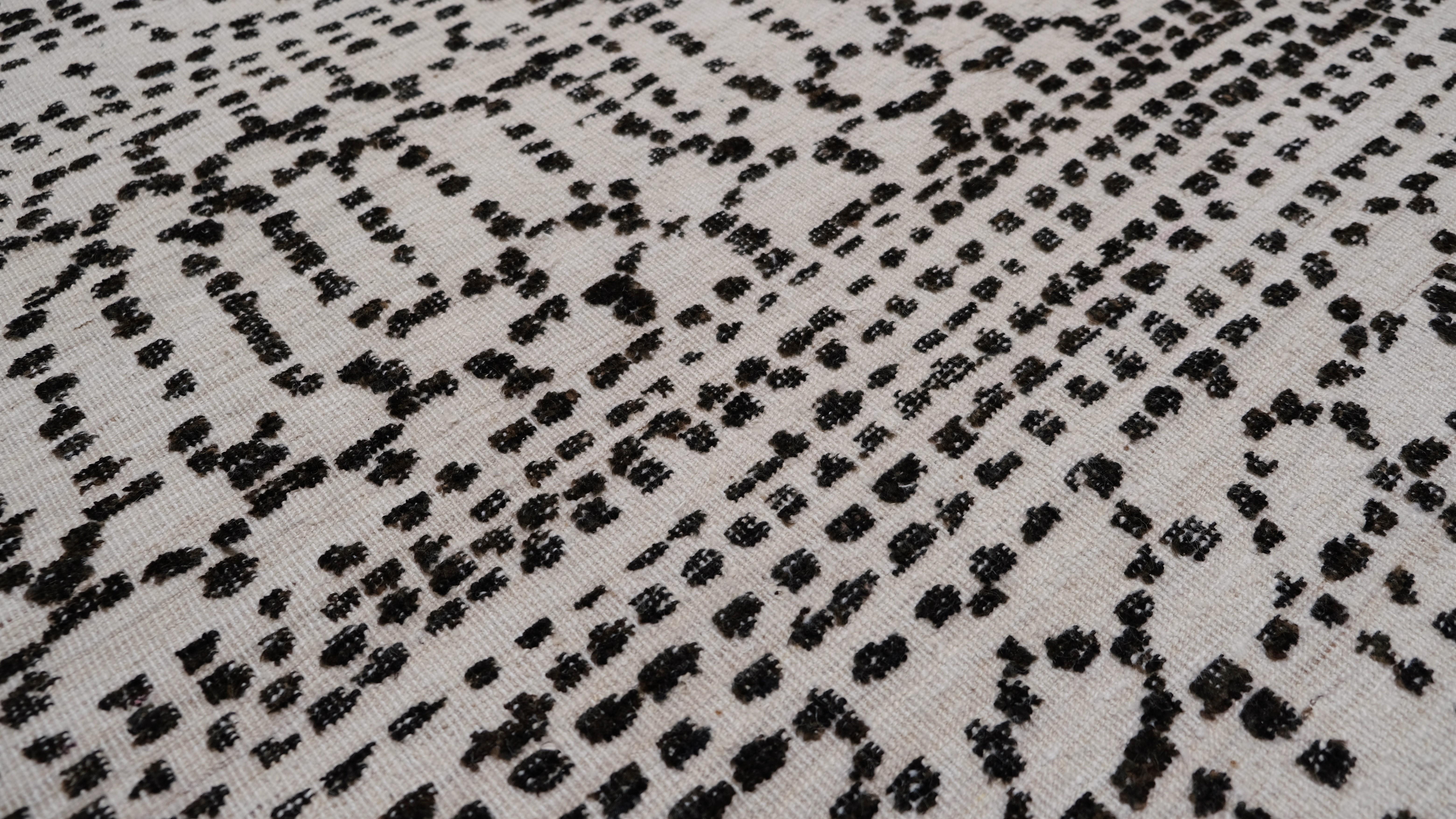 Questo tappeto in lana annodato a mano presenta un sorprendente motivo tribale monocromatico in una raffinata tavolozza nera e avorio. Ispirato ai motivi tradizionali berberi e marocchini, l'intricato design lineare a puntini crea un ritmo