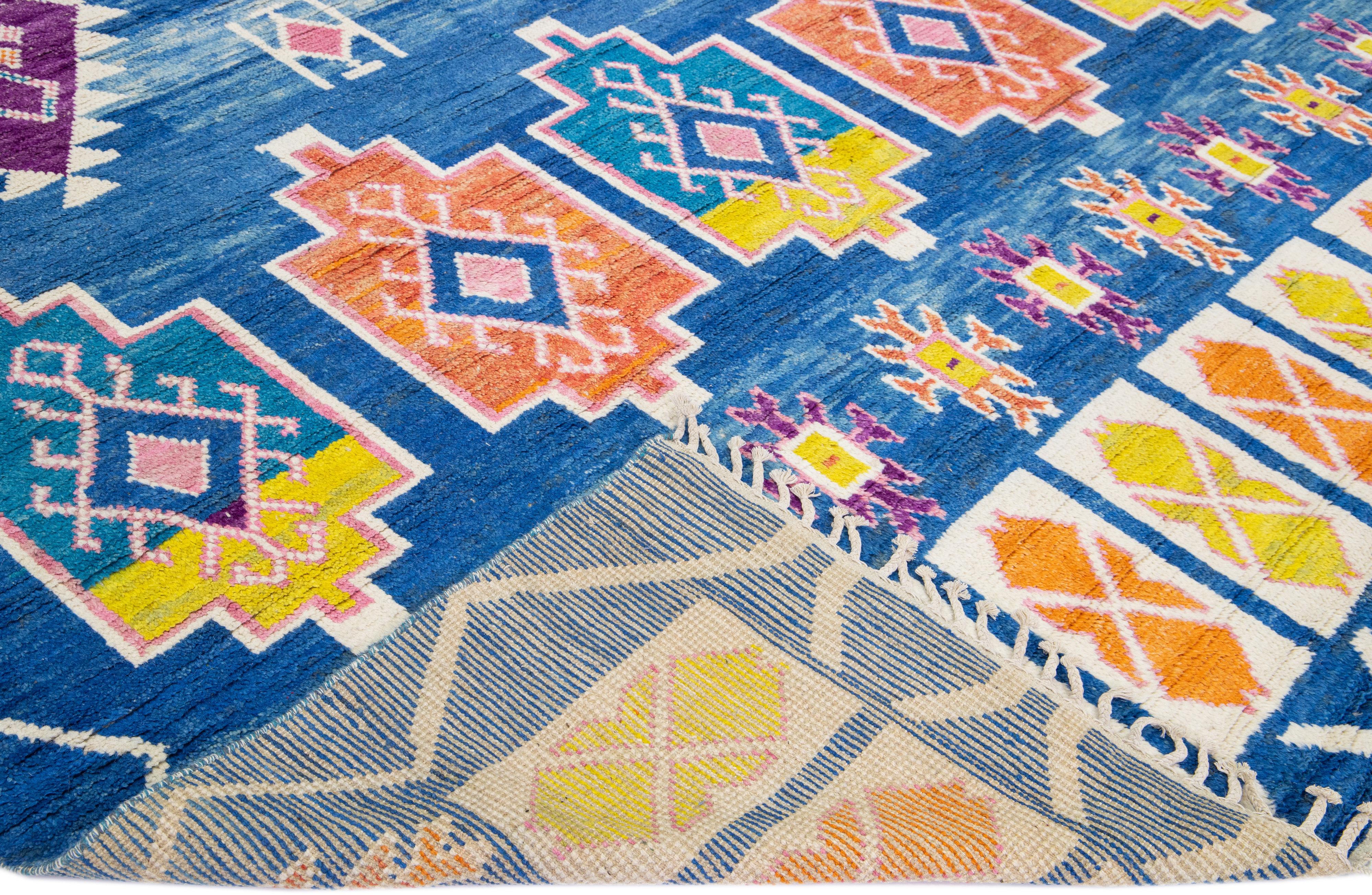 Beautiful modern Moroccan style hand-knotted wool rug with a blue field. This piece has multicolor accent colors in a geometric tribal pattern design with beige fringes on the top and bottom end.

This rug measures: 10' x 14'5