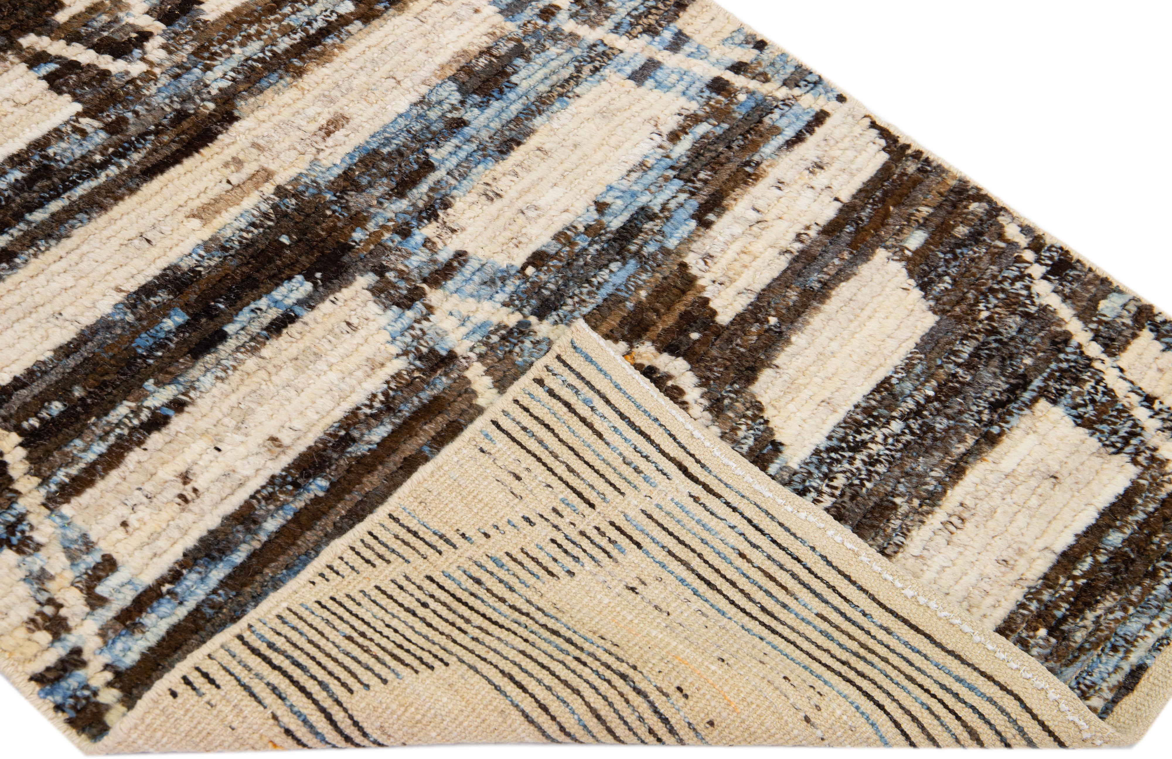 Magnifique tapis en laine fait main de style marocain avec un champ beige et brun. Ce tapis moderne aux accents bleus présente un magnifique motif géométrique tribal sur toute sa surface.

Ce tapis mesure : 2'10