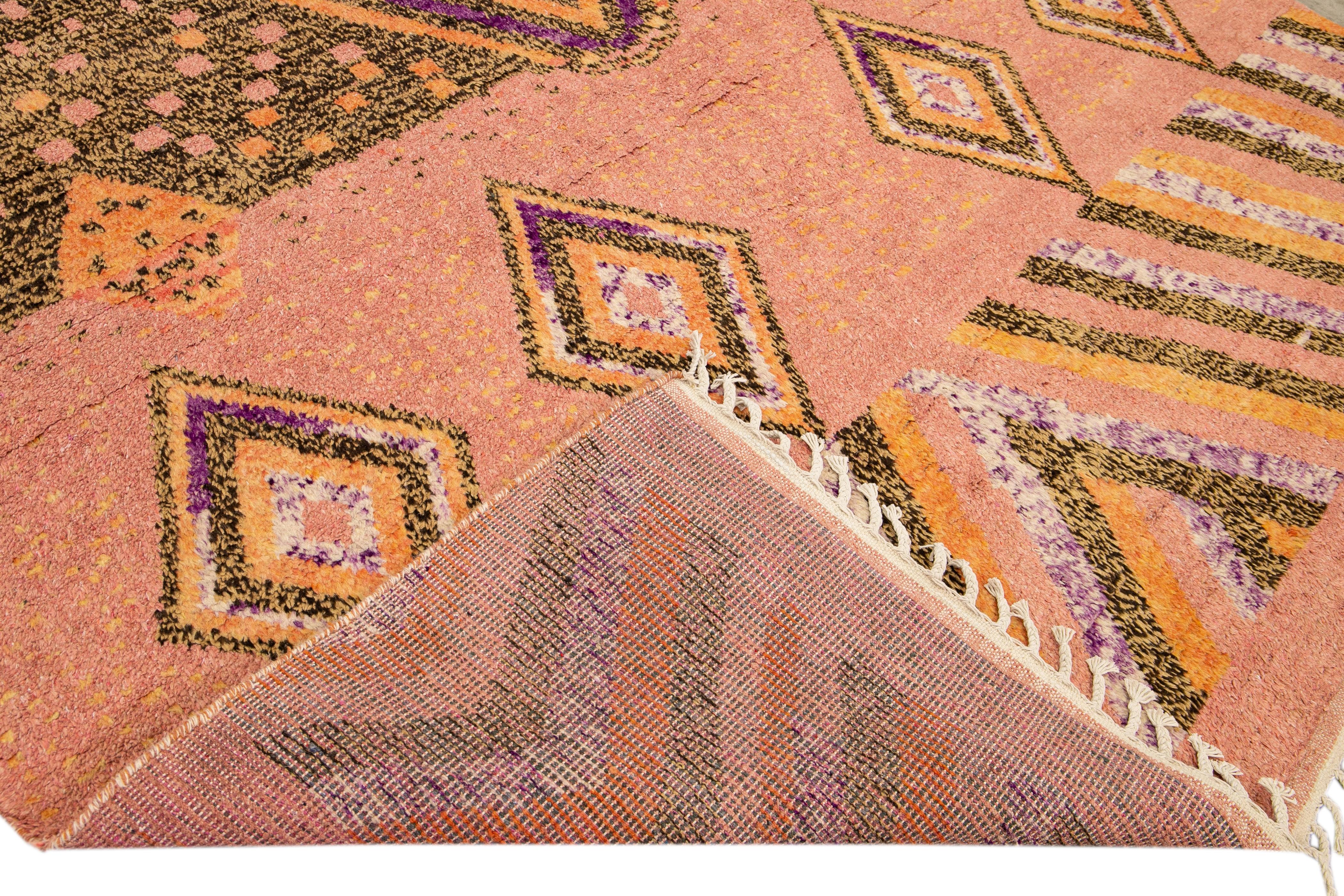 Schöner handgefertigter Wollteppich im marokkanischen Stil mit pfirsichfarbenem Feld. Dieser moderne Teppich mit orangefarbenen, braunen und violetten Akzenten und beigen Fransen hat ein wunderschönes, geometrisches Boho-Muster.

Dieser Teppich