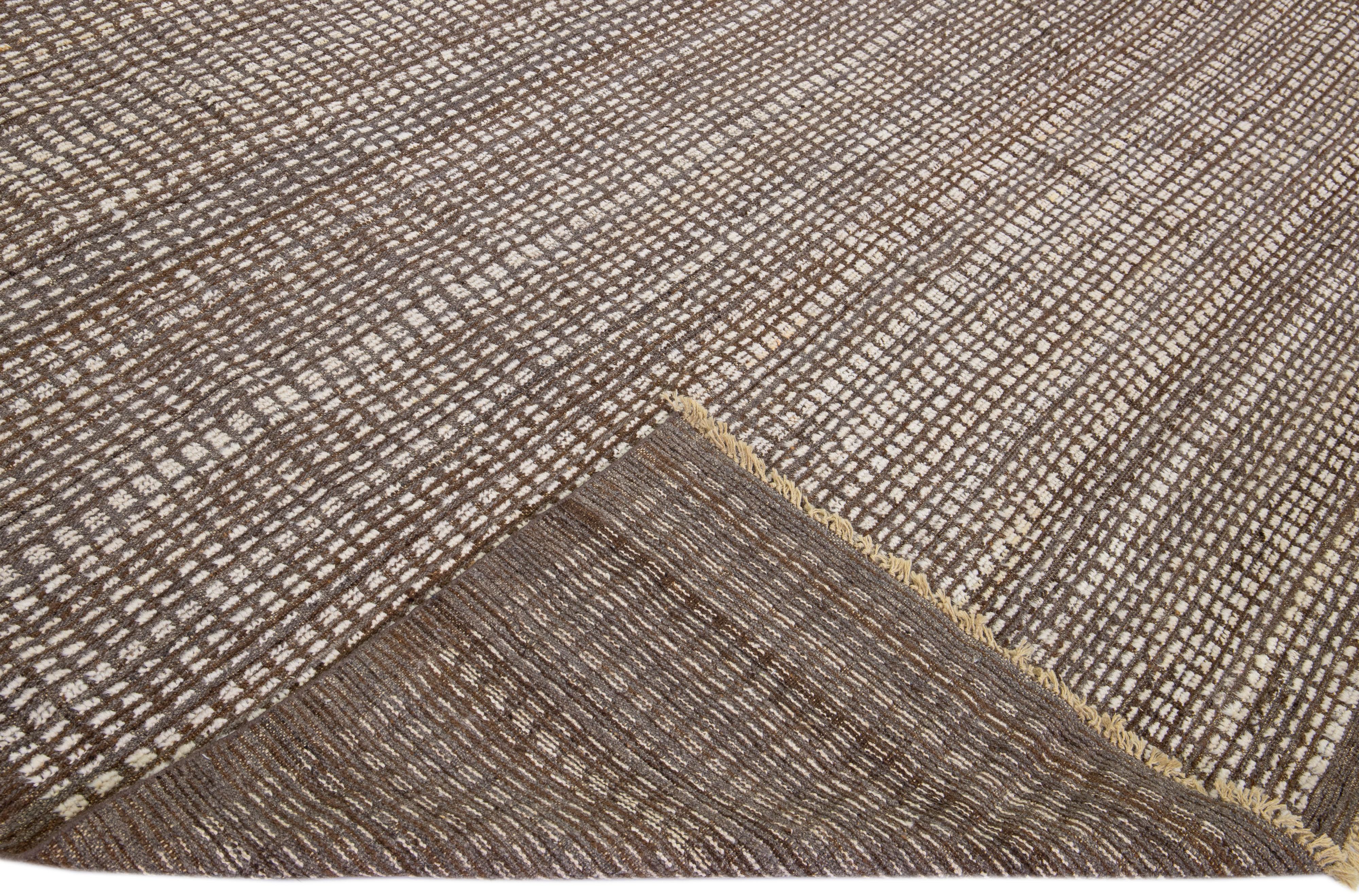 Beautiful modern Moroccan style hand-knotted wool rug with a brown field. This piece has a gorgeous beige subtle geometric pattern design with fringes on the top and bottom end.

This rug measures: 9'5