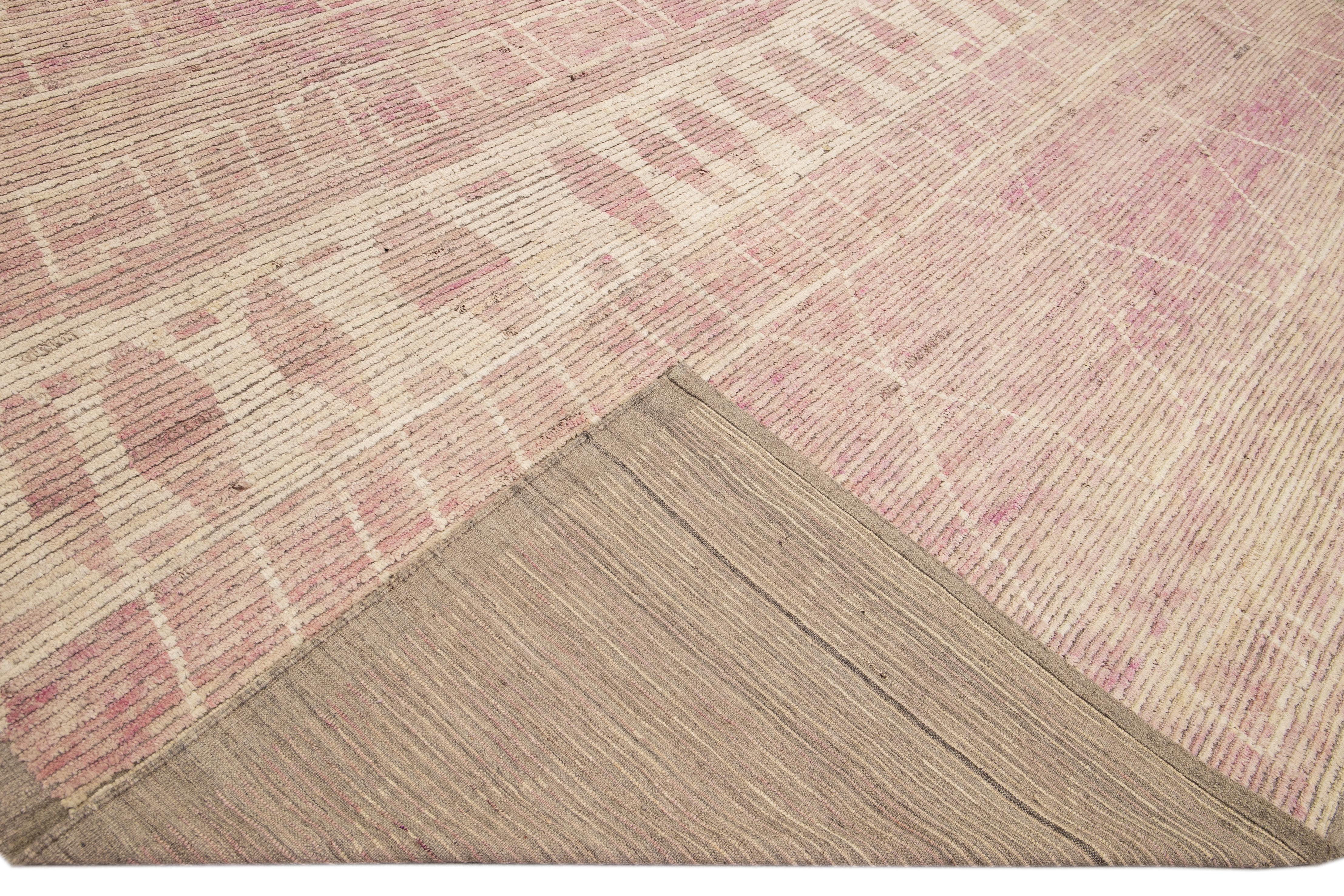Magnifique tapis en laine fait main de style marocain avec un champ beige. Ce tapis moderne aux accents roses et ivoires présente un magnifique motif tribal sur toute sa surface.

Ce tapis mesure : 13'7