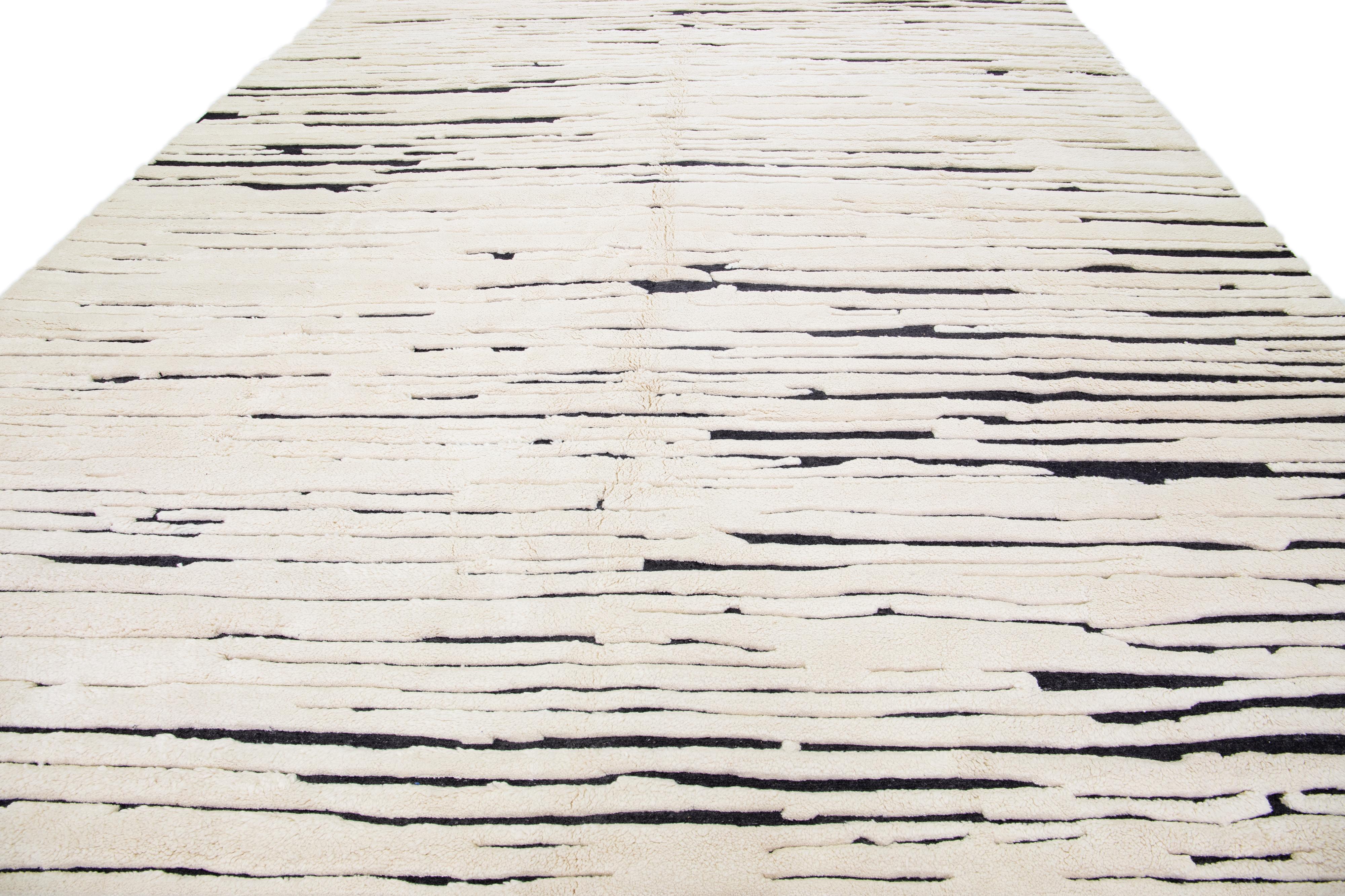 Magnifique tapis en laine fait main de style marocain avec un champ ivoire et noir. Ce tapis moderne présente un magnifique motif à rayures.

Ce tapis mesure : 12'2