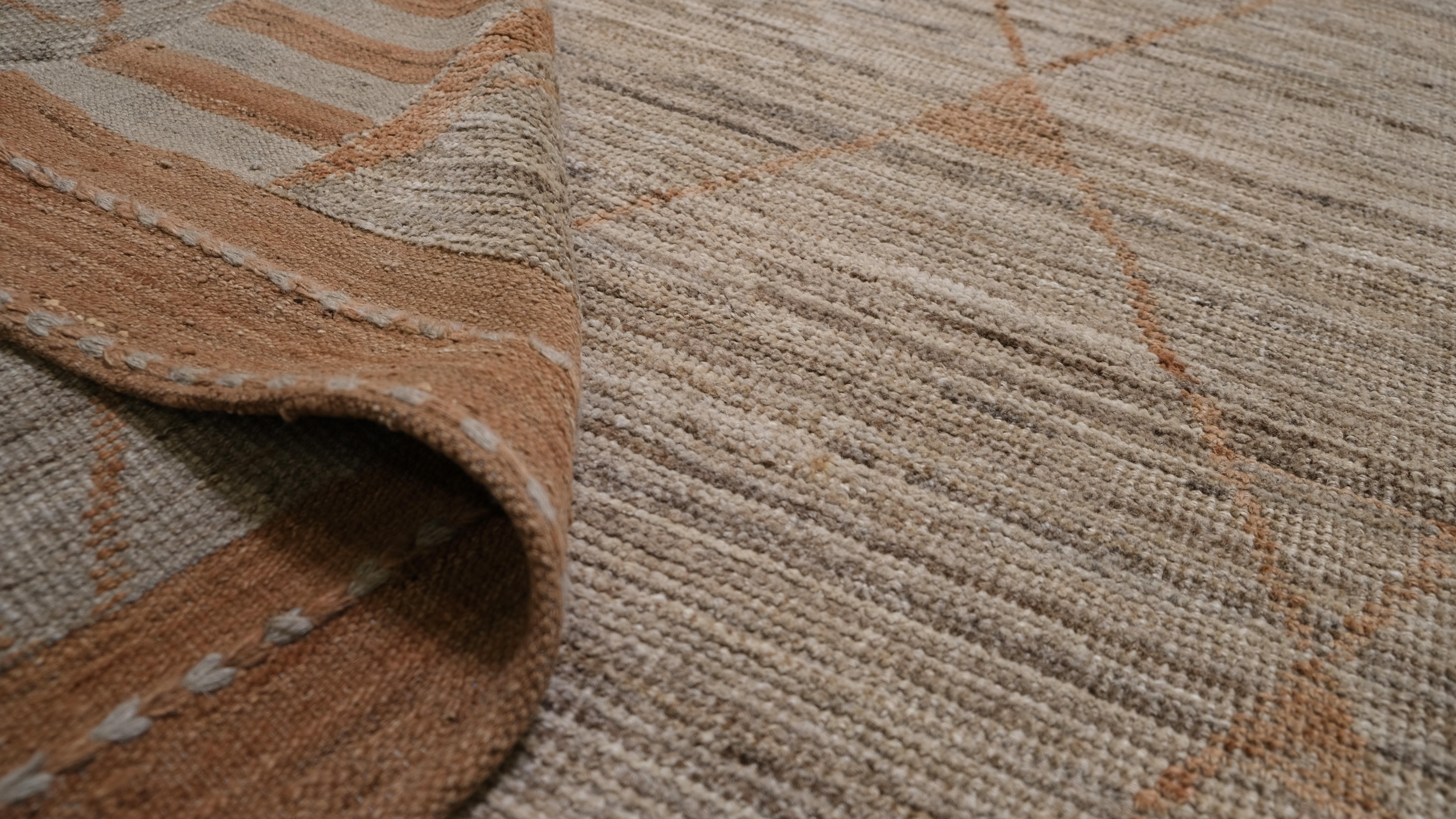 Ce tapis en laine noué à la main est une interprétation moderne des motifs tribaux traditionnels, présentant un motif de treillis en losange avec des accents géométriques subtils. Les tons beige, marron et orange se marient harmonieusement avec la