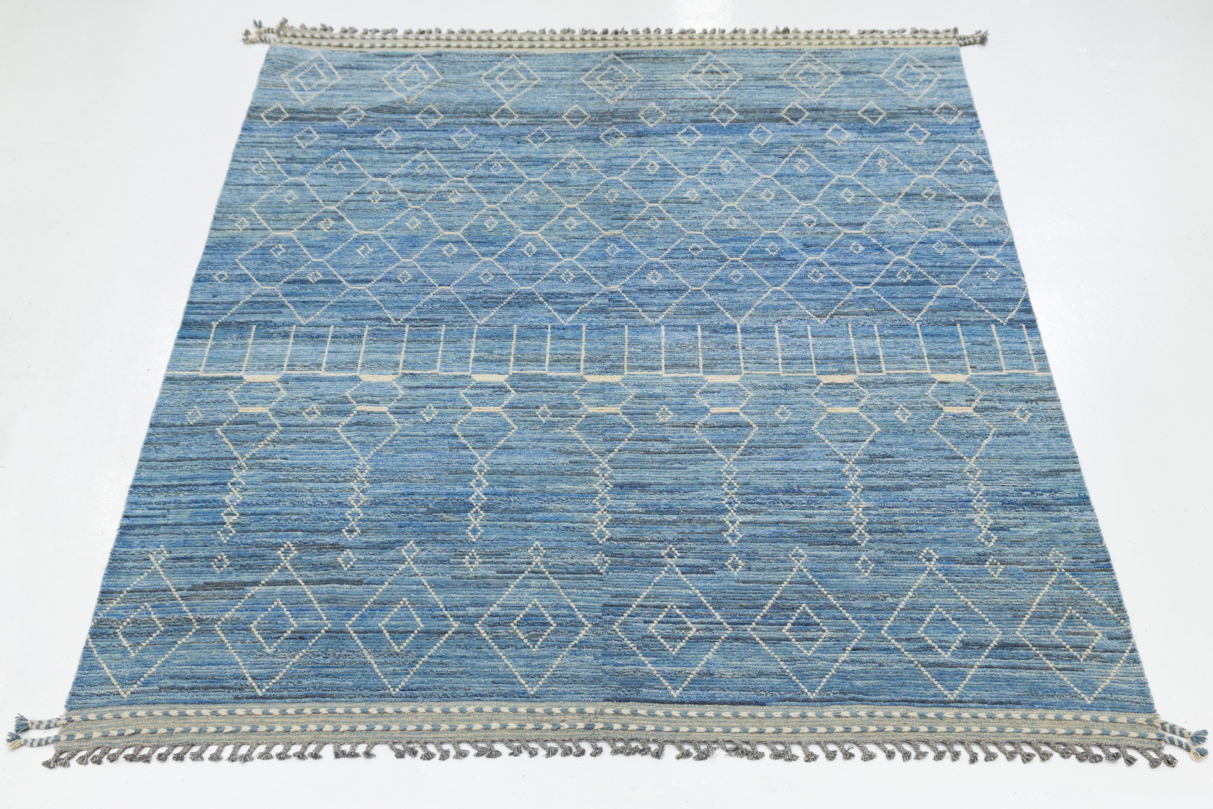 This modern wool rug features a striking interplay of white geometric motifs across a rich blue gradient field. The symmetrical diamond and linear patterns evoke tribal symbolism with a contemporary twist, while fringe edges add artisanal charm. A