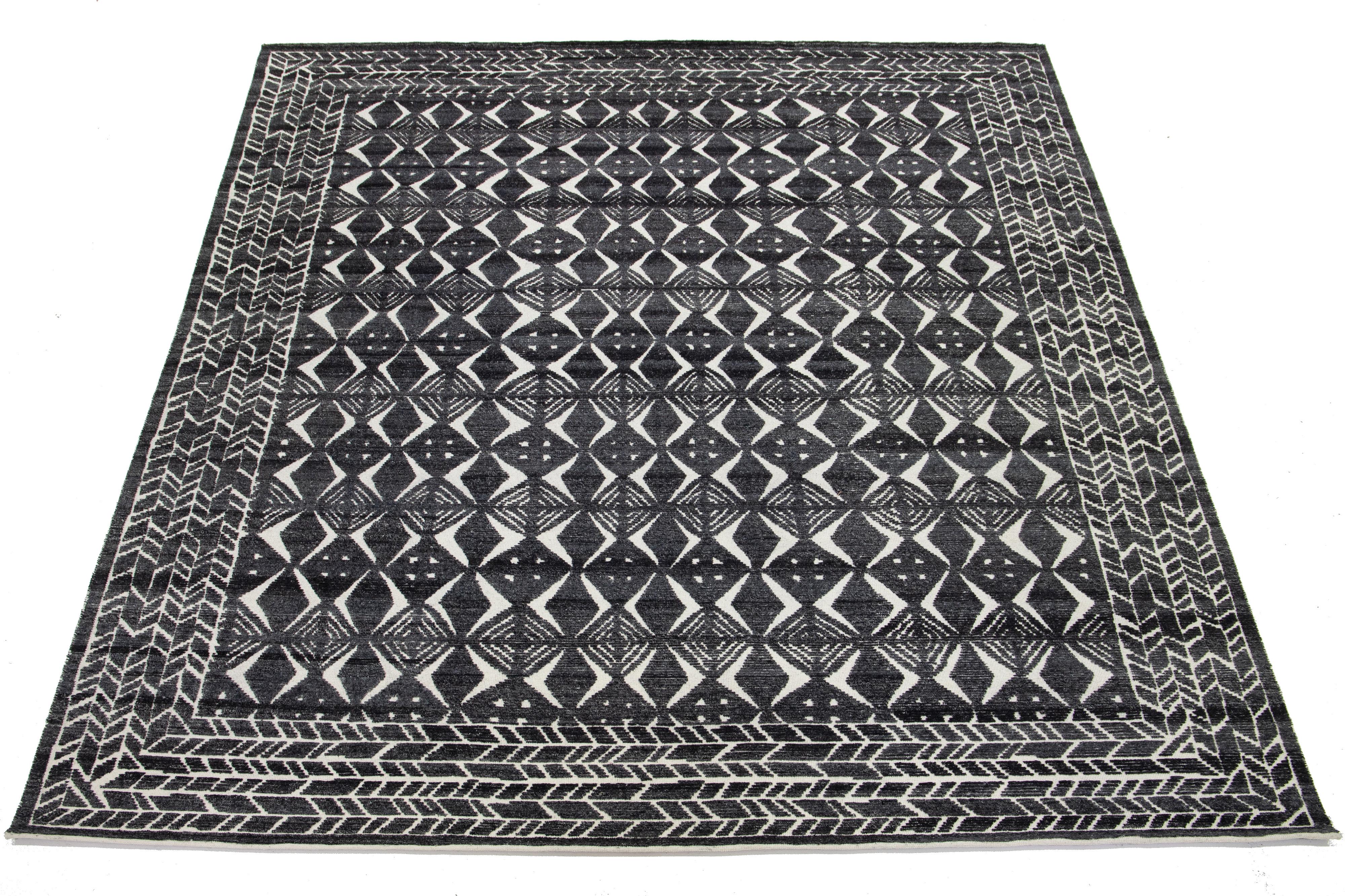 Dieser moderne, handgeknüpfte Wollteppich im marokkanischen Stil zeichnet sich durch ein sattes, kohlegraues und elfenbeinfarbenes Feld aus, das mit einem fesselnden geometrischen Muster verziert ist. Dieses atemberaubende Stück wird die Ästhetik