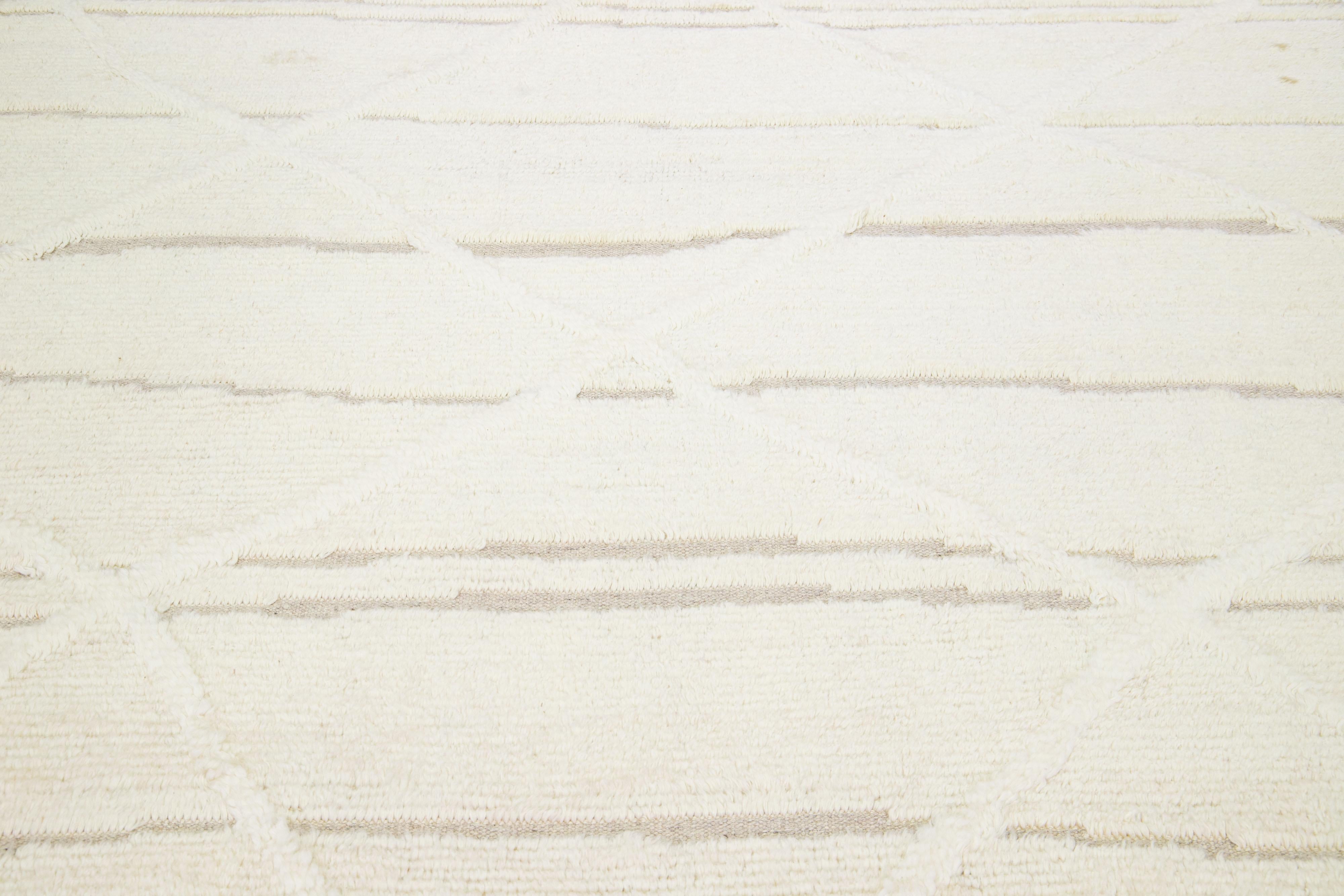 Questo tappeto in lana annodato a mano presenta un design marocchino contemporaneo, che combina abilmente linee serene e sofisticate su un incantevole sfondo avorio/crema. L'integrazione dei colori crea una disposizione geometrica tribale di grande