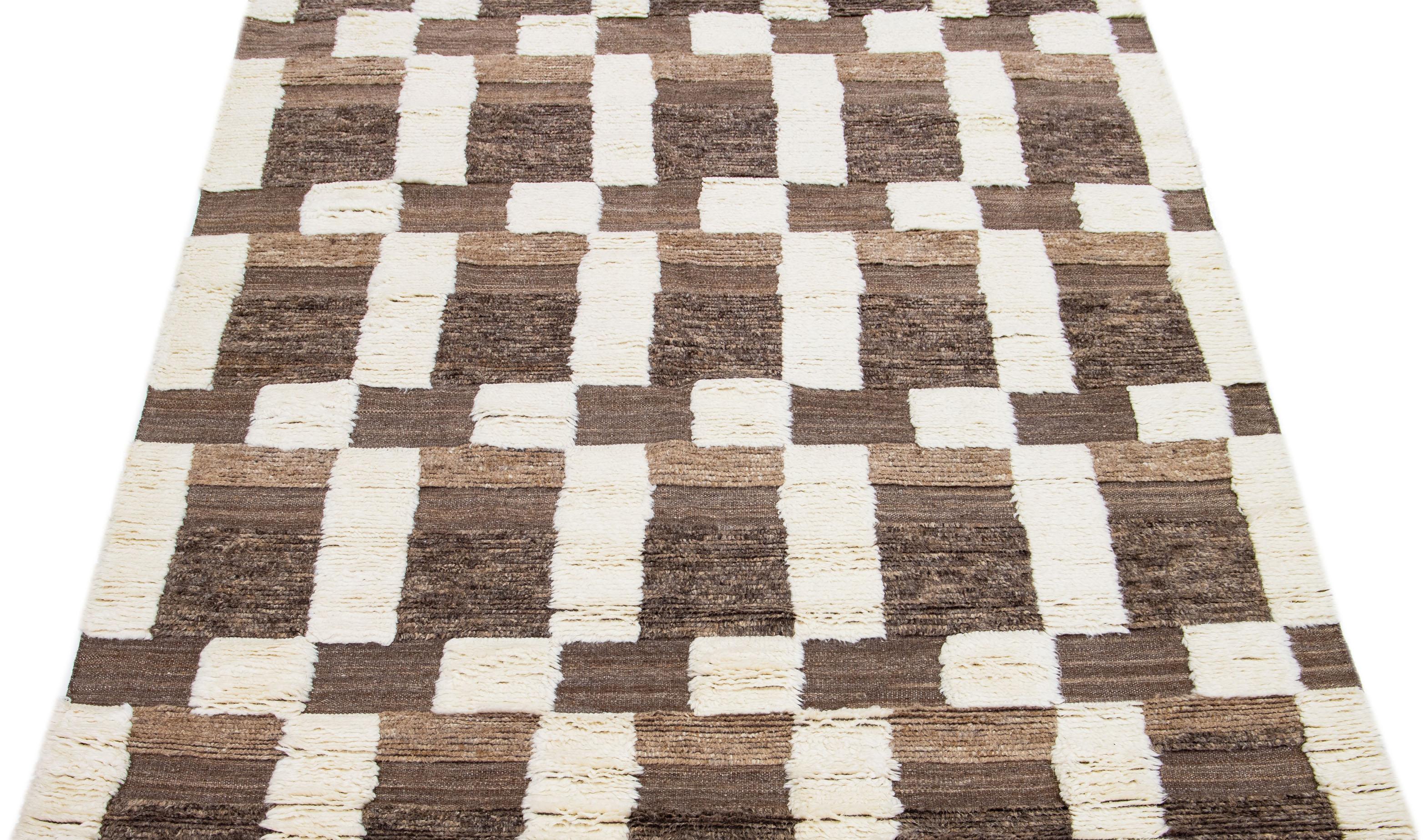This beautifully made wool rug showcases a contemporary Moroccan pattern in a calming Ivory shade, artfully set against a captivating brown background. The perfect harmony between these colors creates a flawless abstract arrangement that leaves an
