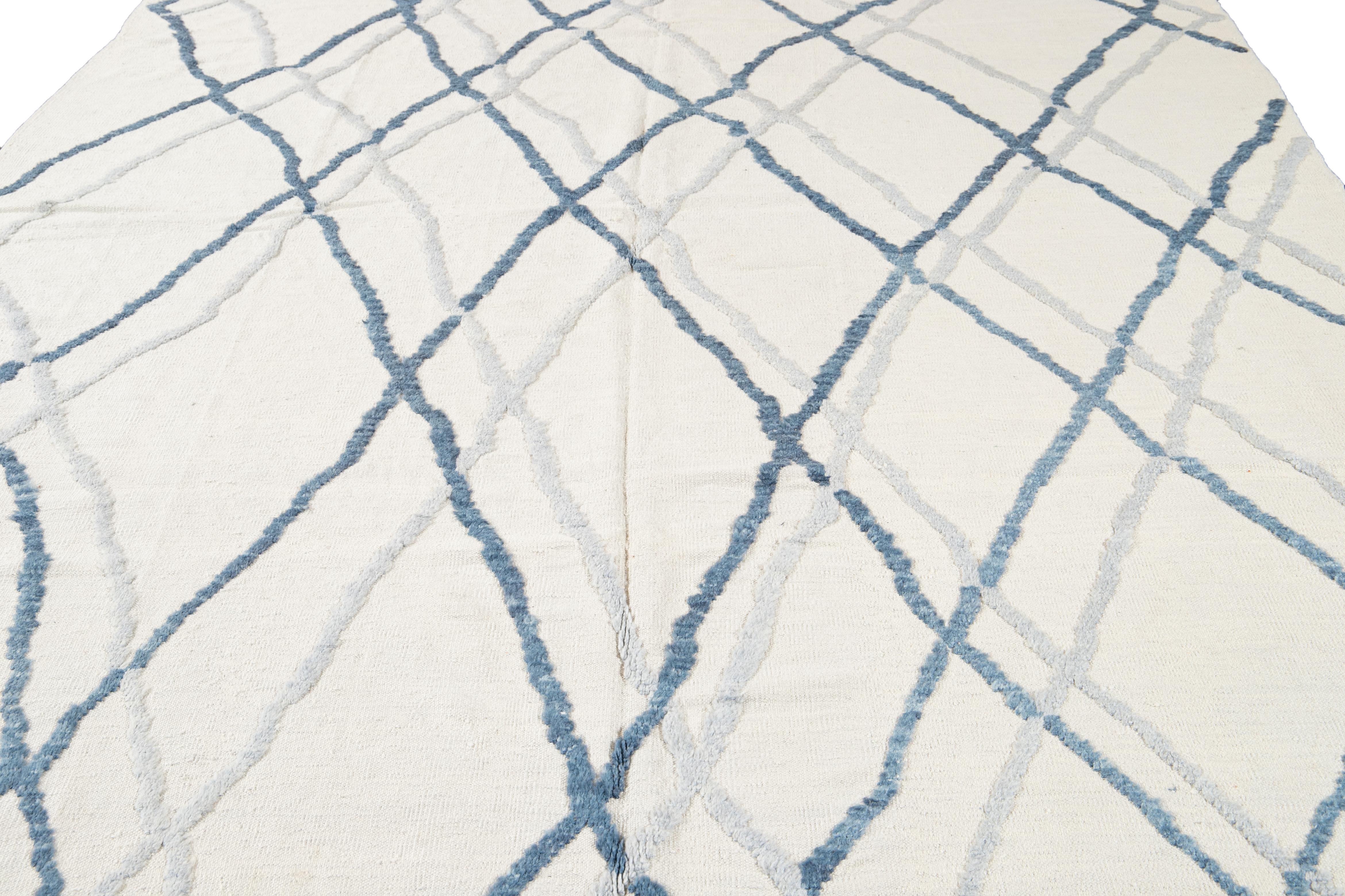 The mesmerizing Moroccan pattern showcased on this hand-knotted wool rug exudes a contemporary allure in blue hues with a captivating ivory background. Its visually stunning Tribal design creates a captivating contrast, perfectly complementing any