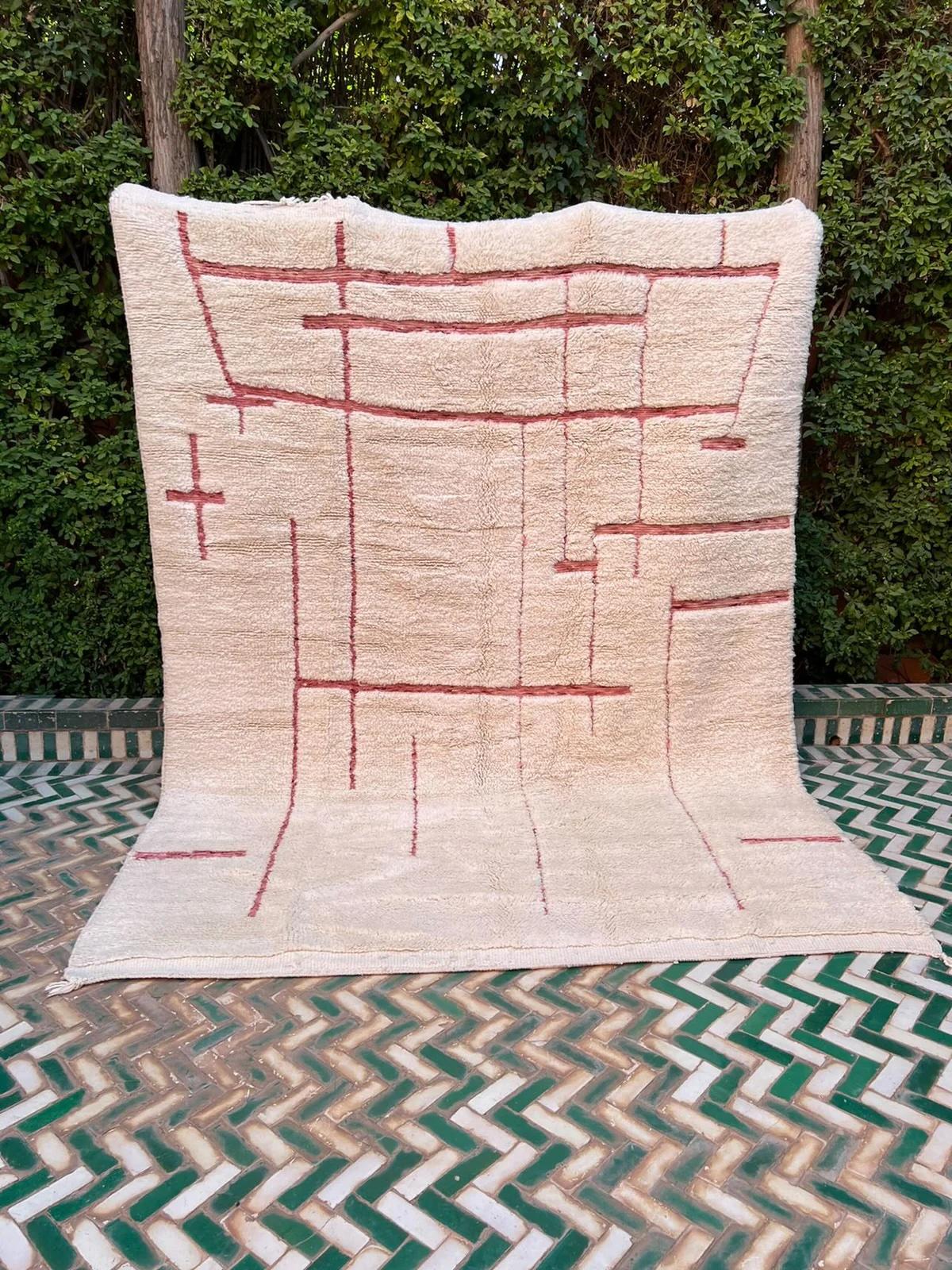 Questo tappeto marocchino di medie dimensioni, color crema, è stato realizzato a mano su un telaio tradizionale da abili artigiani nelle montagne dell'Atlante. È realizzato con lana M'Rirt, ultra lussuosa e di alta qualità. Si tratta di un perfetto