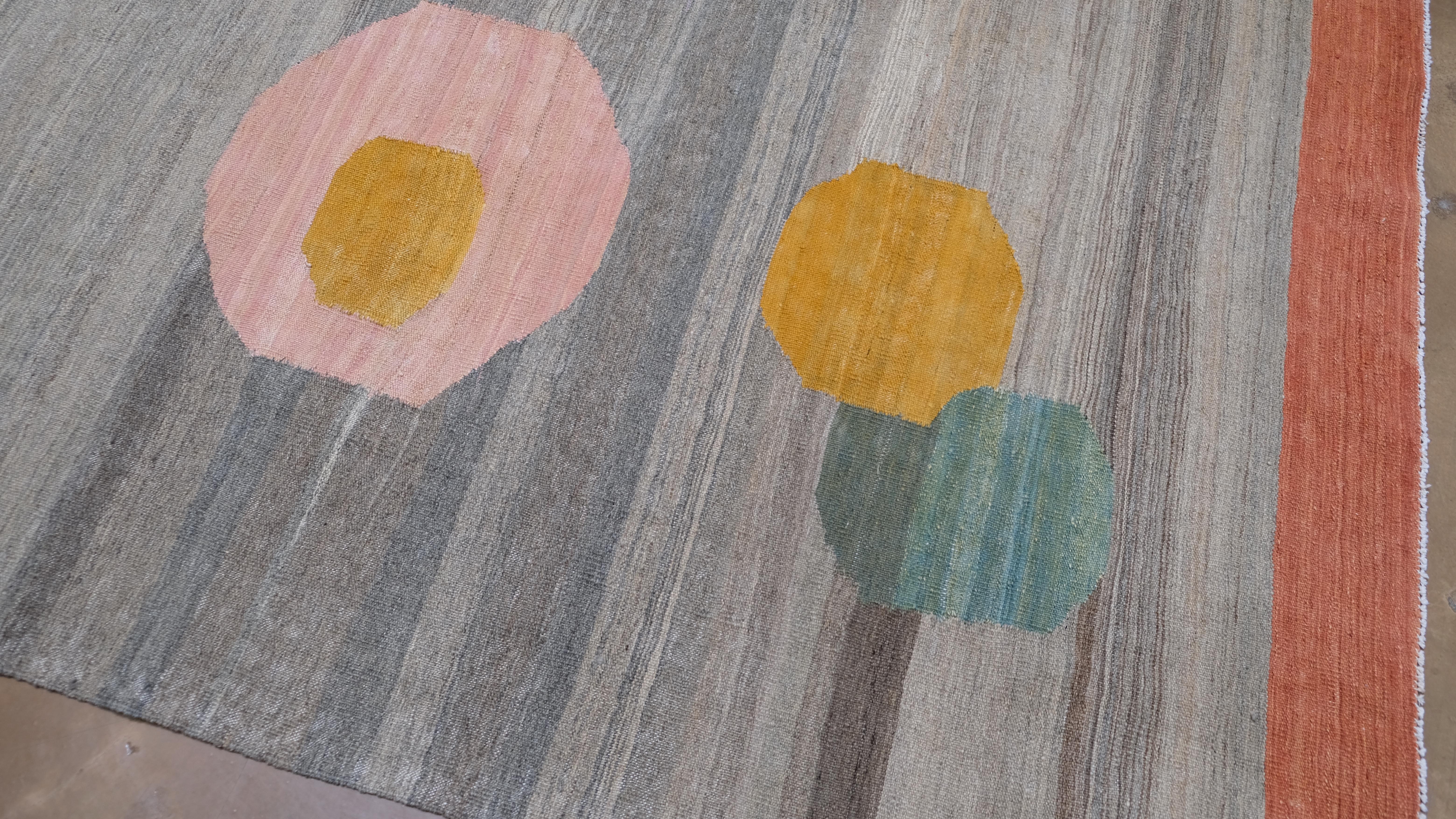 Dieser handgewebte Wollteppich zeigt ein verspieltes und zugleich raffiniertes geometrisches Tupfenmuster, das moderne Ästhetik und traditionelle Handwerkskunst nahtlos miteinander verbindet. Der Teppich hat einen neutralen, grau getönten