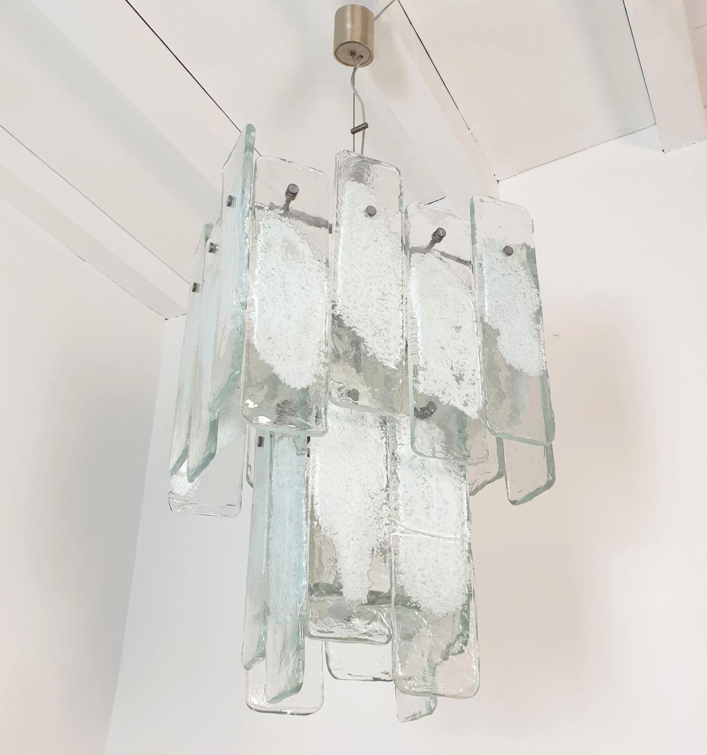 Gran araña geométrica de cristal de Murano Mid Century Modern de Mazzega, Italia, años 70.
La lámpara colgante vintage está formada por un armazón cromado y piezas rectangulares de cristal de Murano transparente y blanco.
El vidrio es grueso y de