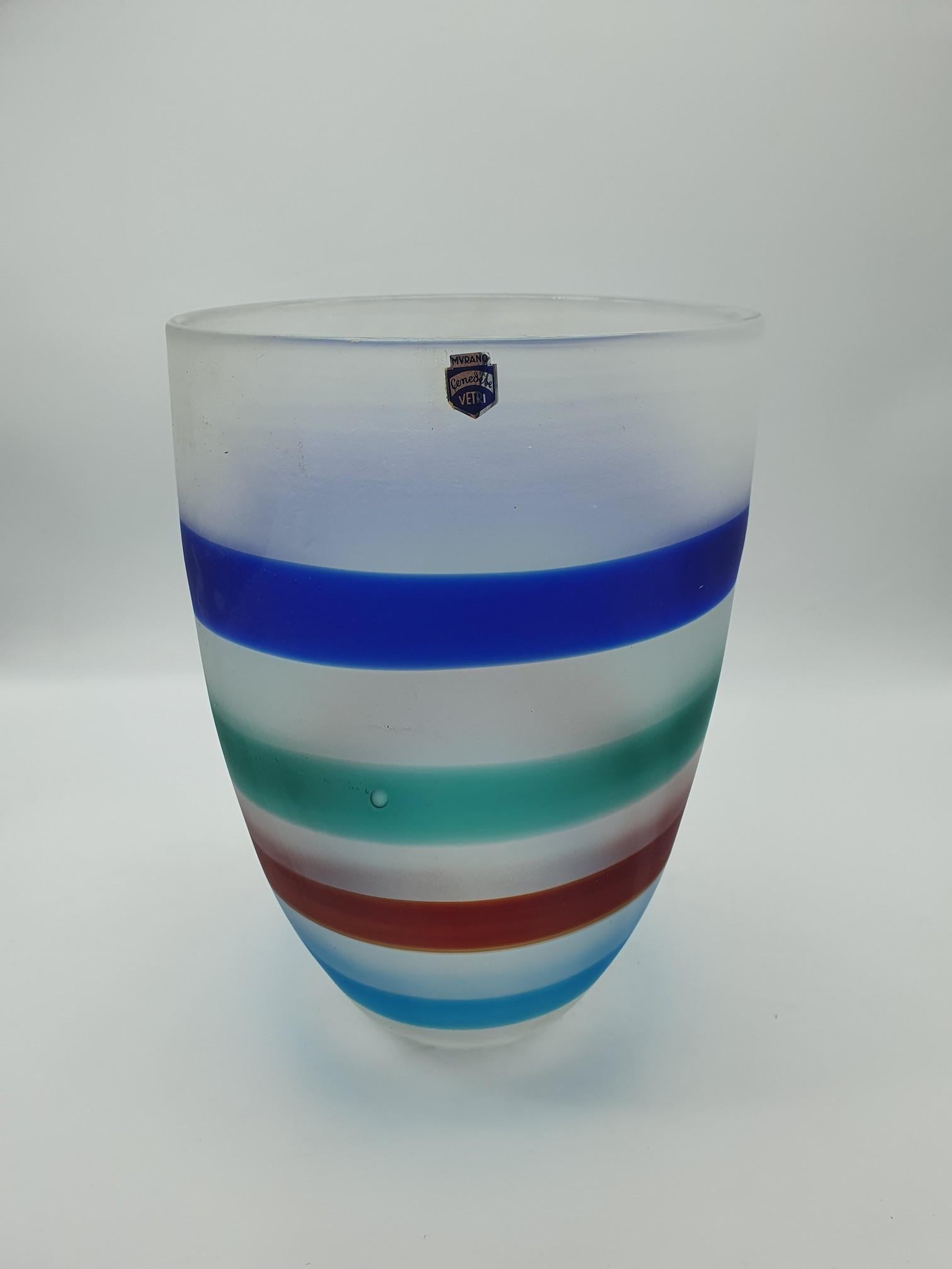 This great vase from Gino Cenedese e Figlio was made in the early 1990s, and features multicolored bands (blue, green, red and tourquoise) on a whitish background. The vase is completely handmade and mouth-blown in Murano, and the matte effect comes