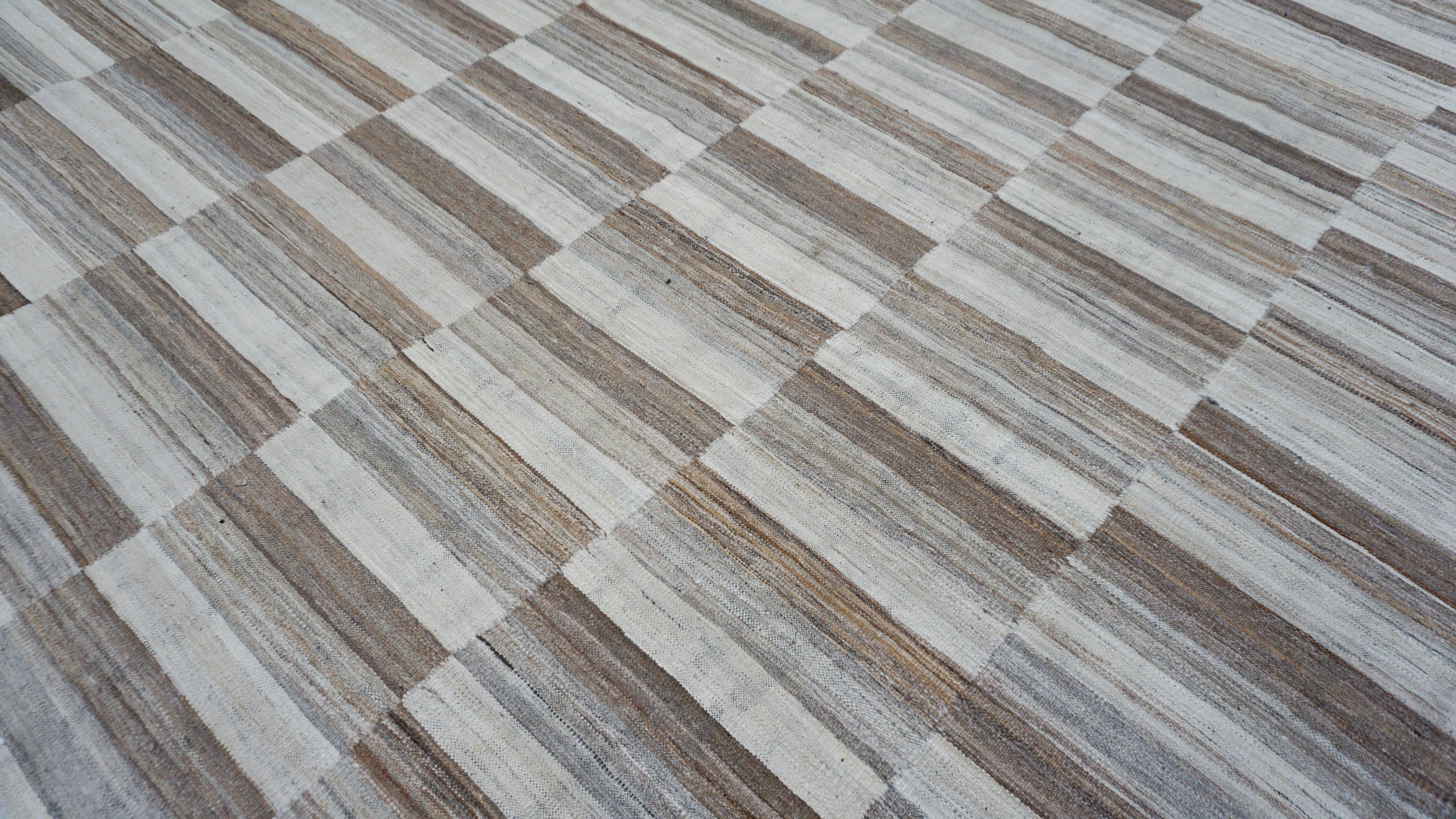 This handwoven wool kilim is a bold celebration of linear geometry and organic materials. The color palette ranges from ivory, beige, brown, reflecting the natural wool colors with just enough tonal contrast to create a modern checker effect.