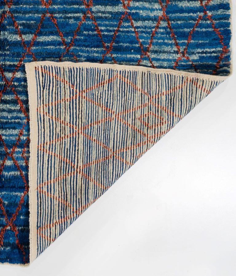 An eye-catching Moroccan design contemporary hand-knotted organic wool rug. It gives off a shimmering look of darker and lighter shades of blue with a red net cast over it.

This beautifully rendered plush carpet is made entirely of hand-spun