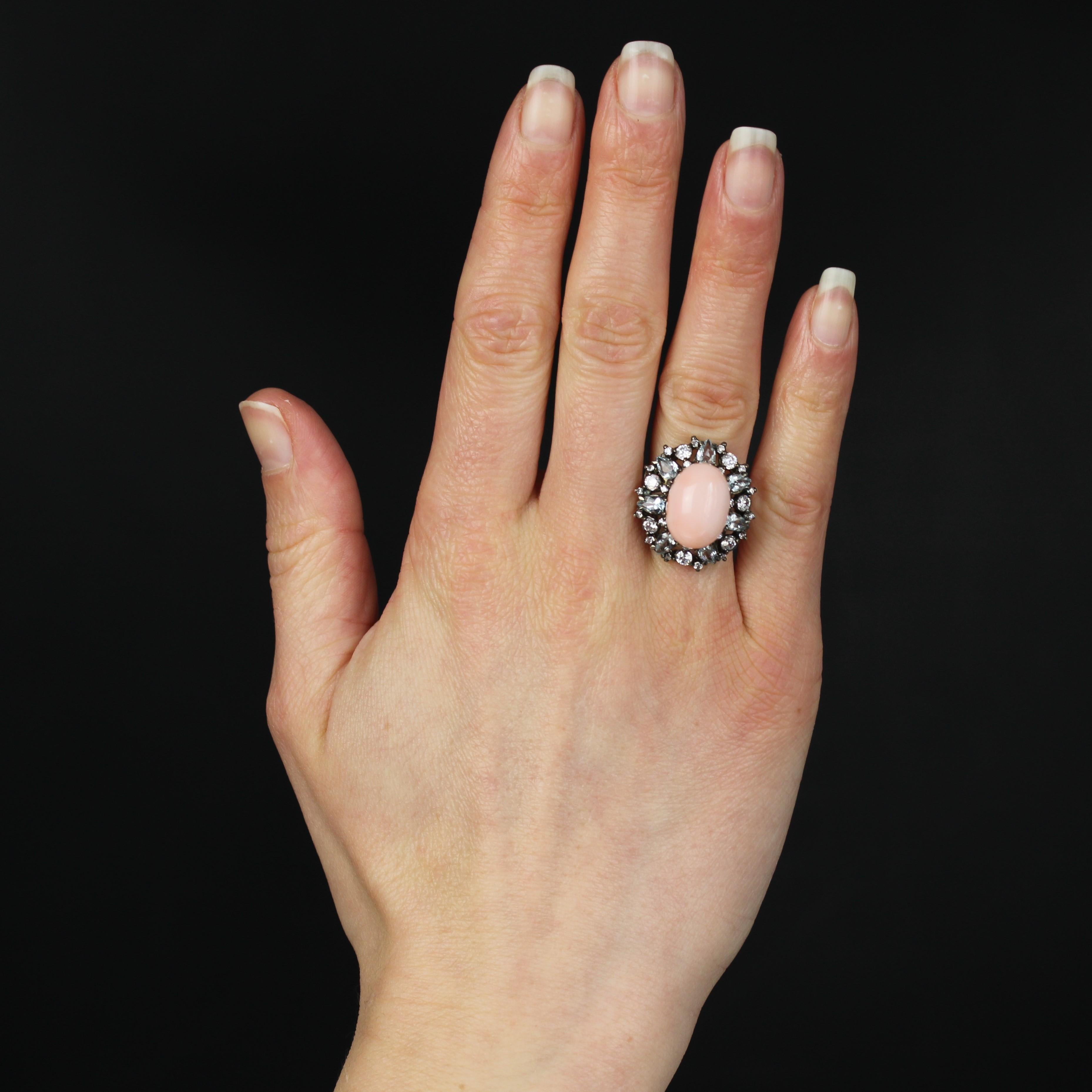 Ring in silver.
This important cocktail ring features an angel-skin coral cabochon in the center, held in place with claws. The coral is surrounded by alternating pear-cut aquamarines and small zirconium crystals of different sizes. The basket is