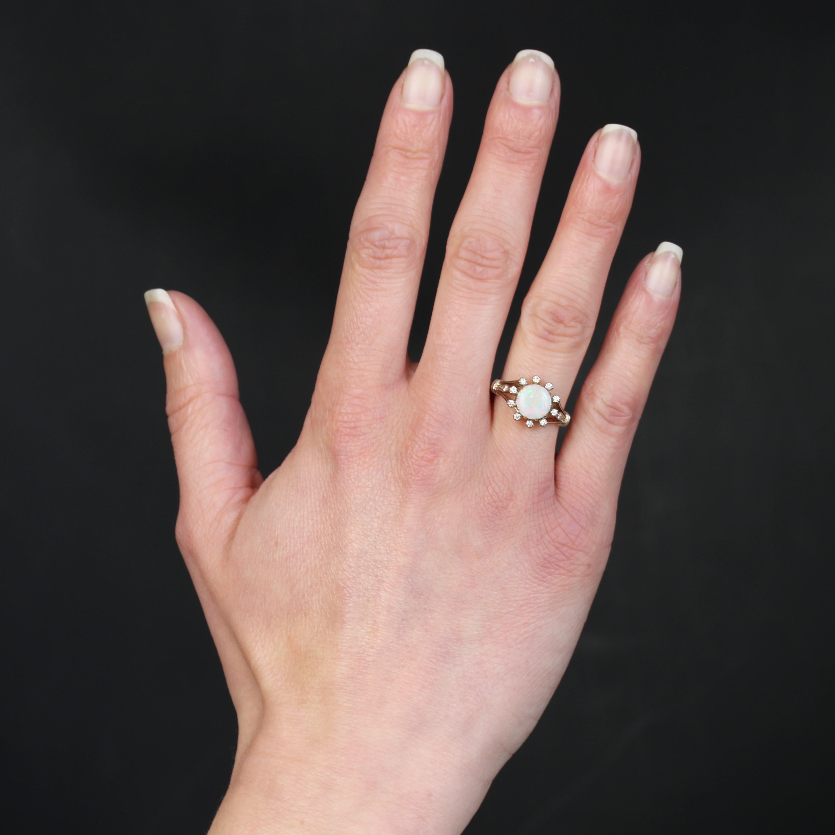 Ring in 18 karat white gold.
This charming vintage-style ring features a cabochon-cut round opal from Australia in the center, held in place with claws. It is surrounded by 10 modern brilliant-cut diamonds set in claws. The start of the ring is