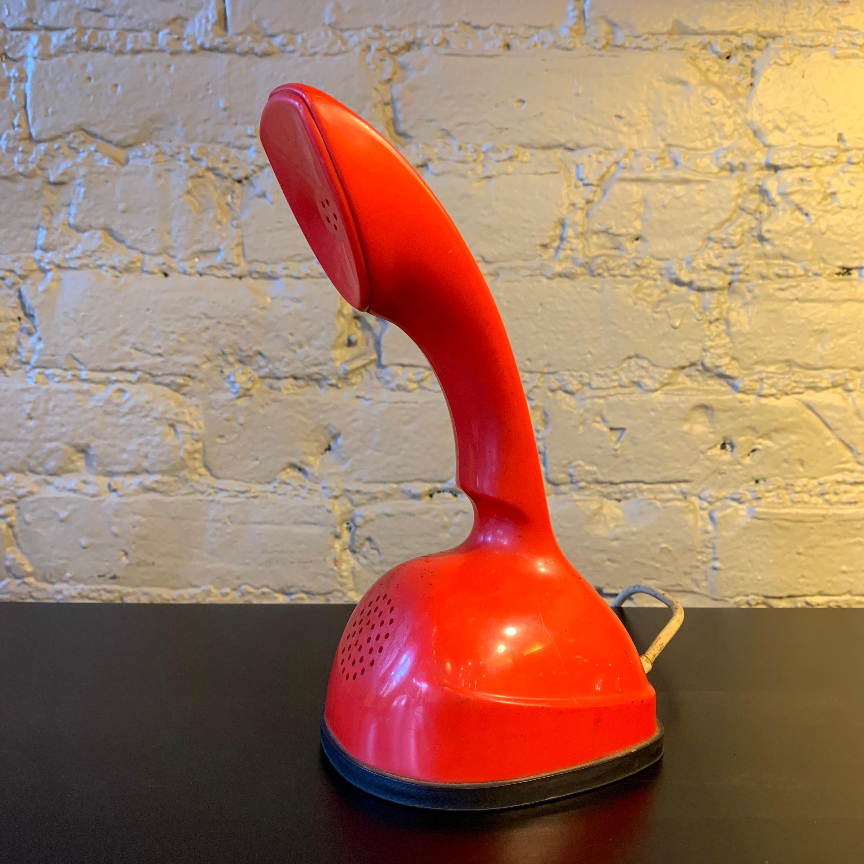Red, modern one-piece Ericofon telephone created by the Ericsson Company of Sweden and manufactured by North Electric in Galion, Ohio features a rotary dial on the bottom. Due to its styling and its influence on future telephone design, the Ericofon