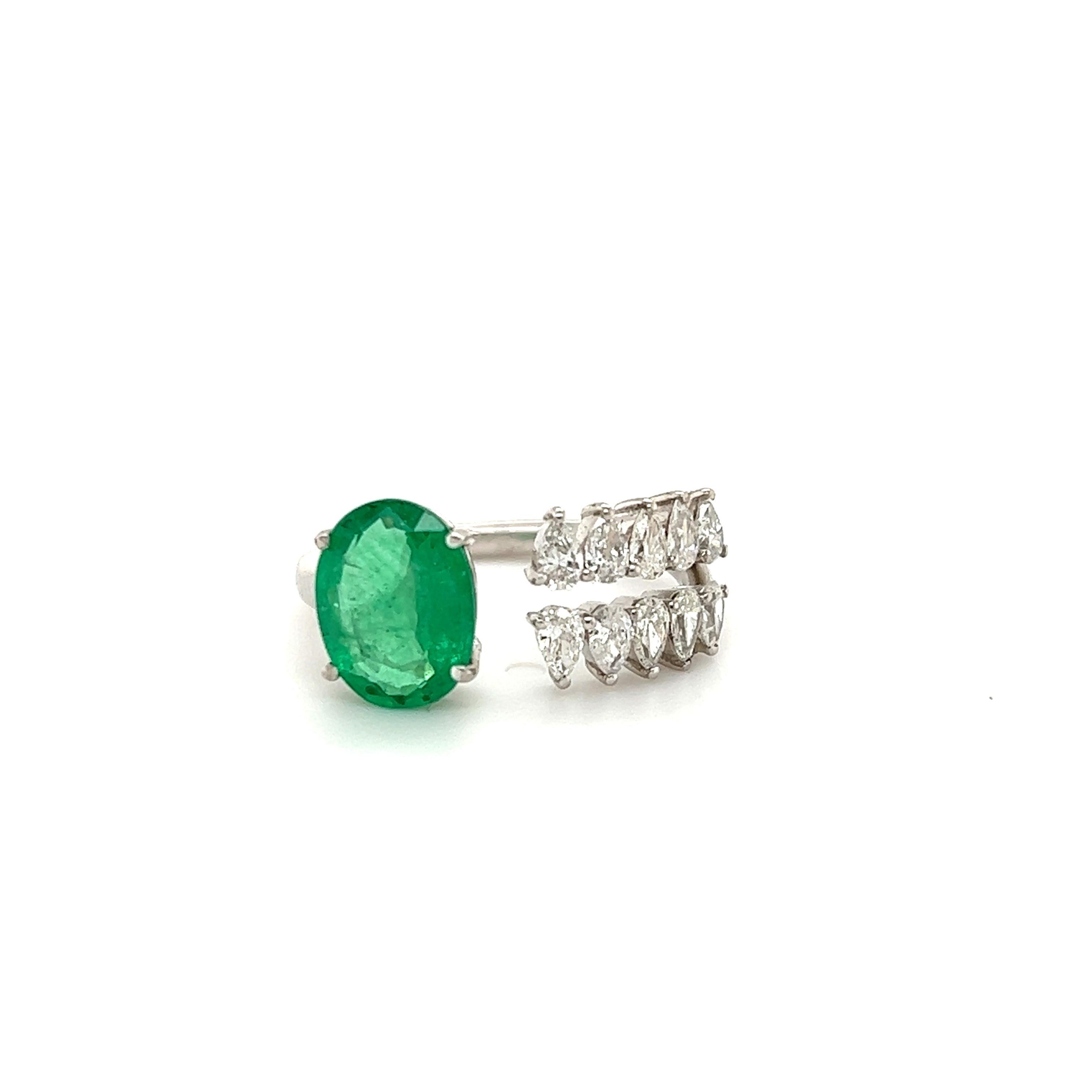 Gorgeous design seen on this ring crafted in 18k white gold. This fantastic design shows pear shape natural diamonds and one vibrant colored green emerald in a oval shape.  The ring is crafted as an open design by-pass ring with diamonds on one side