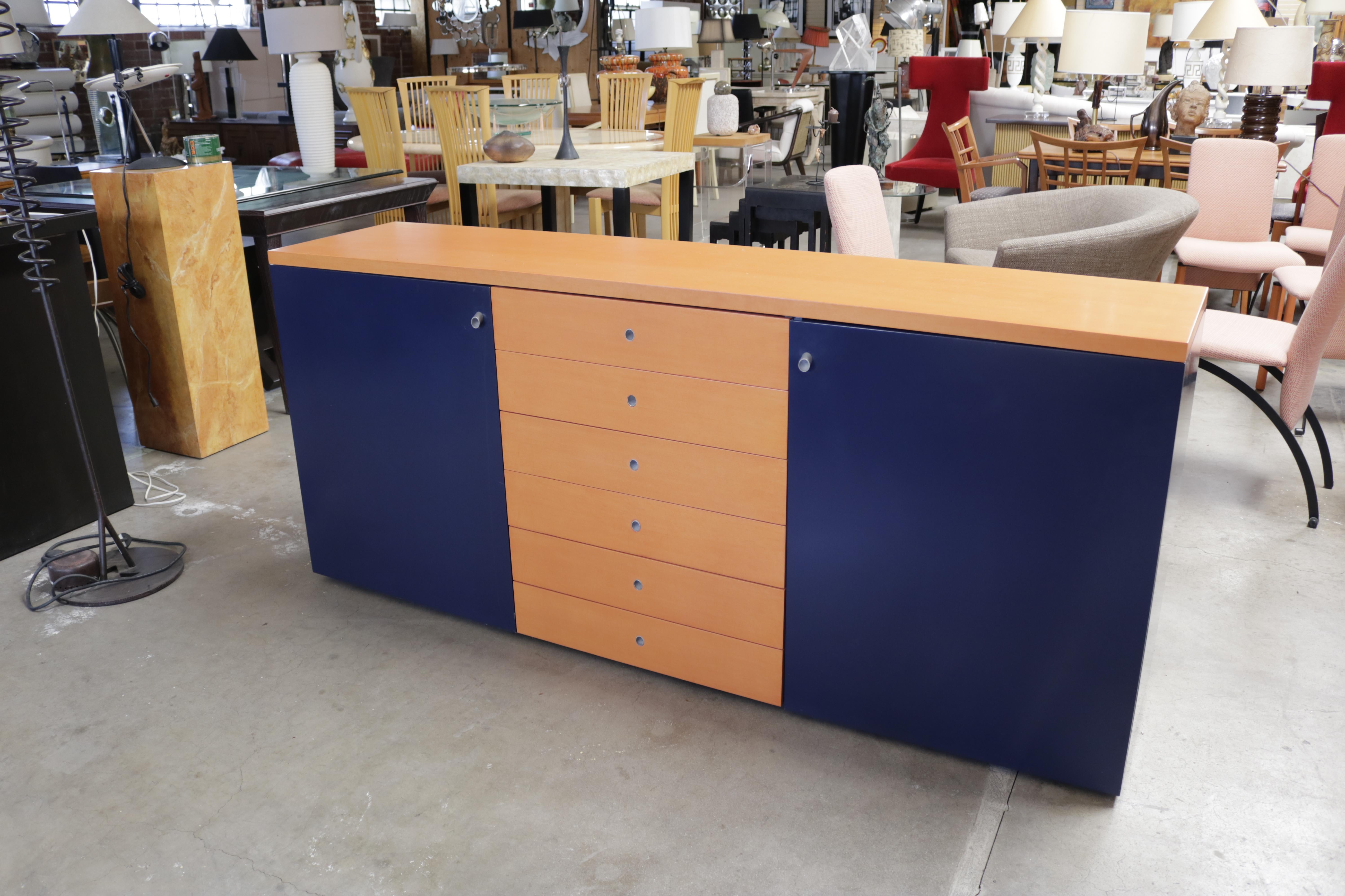 A two-toned buffet in terracotta orange and navy blue stained wood, with brushed steel accented pulls. There are six center drawers. The left side door has 3 shelves and the right side door has 2 shelves.

Manufactured by Castelijn Meubelindustrie