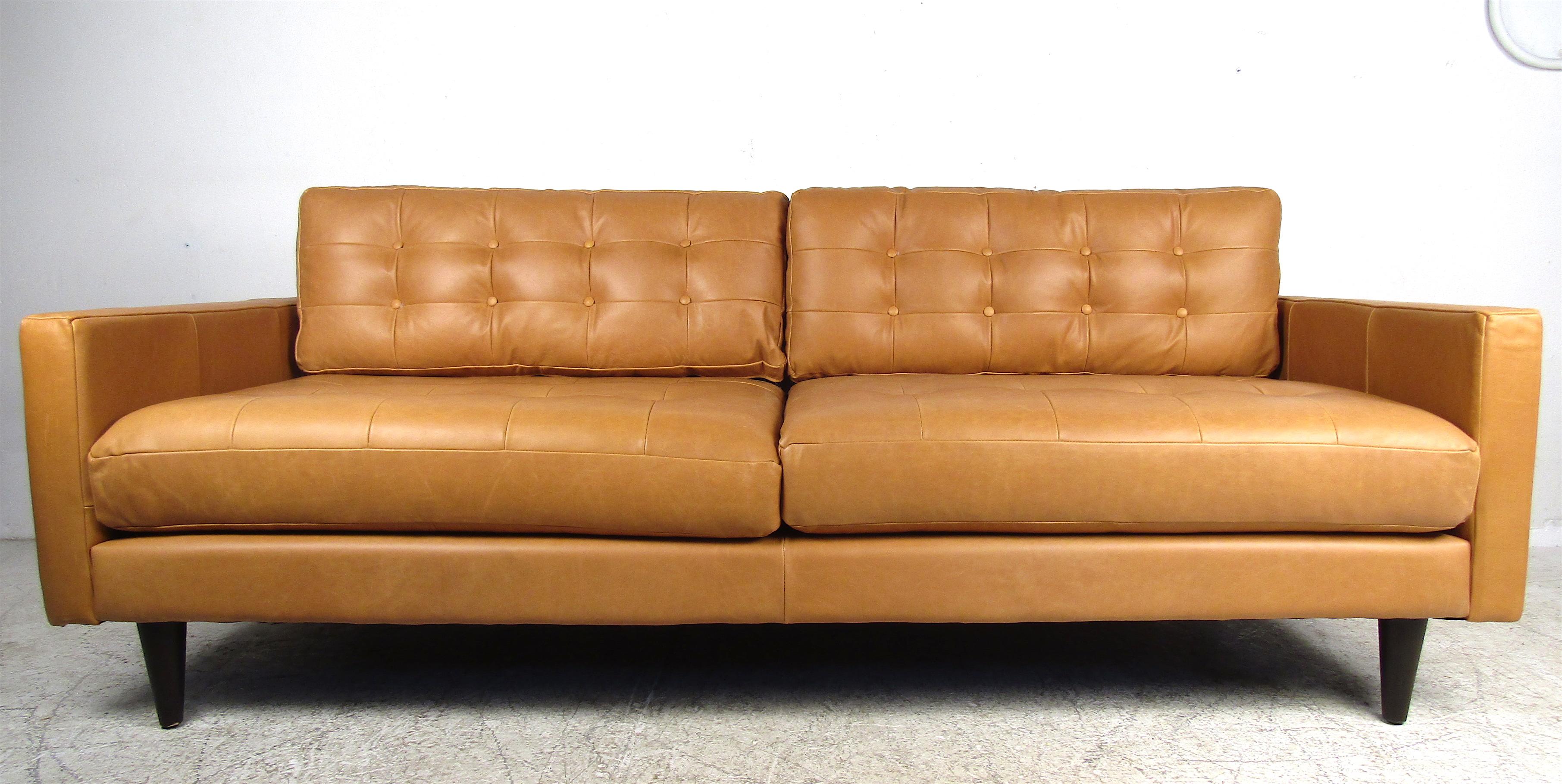 This beautiful contemporary modern sofa features four overstuffed removable tufted cushions. A comfortable a stylish piece that sits on stubby black tapered wood legs. An elaborate orange color that is sure to make a lasting impression in any