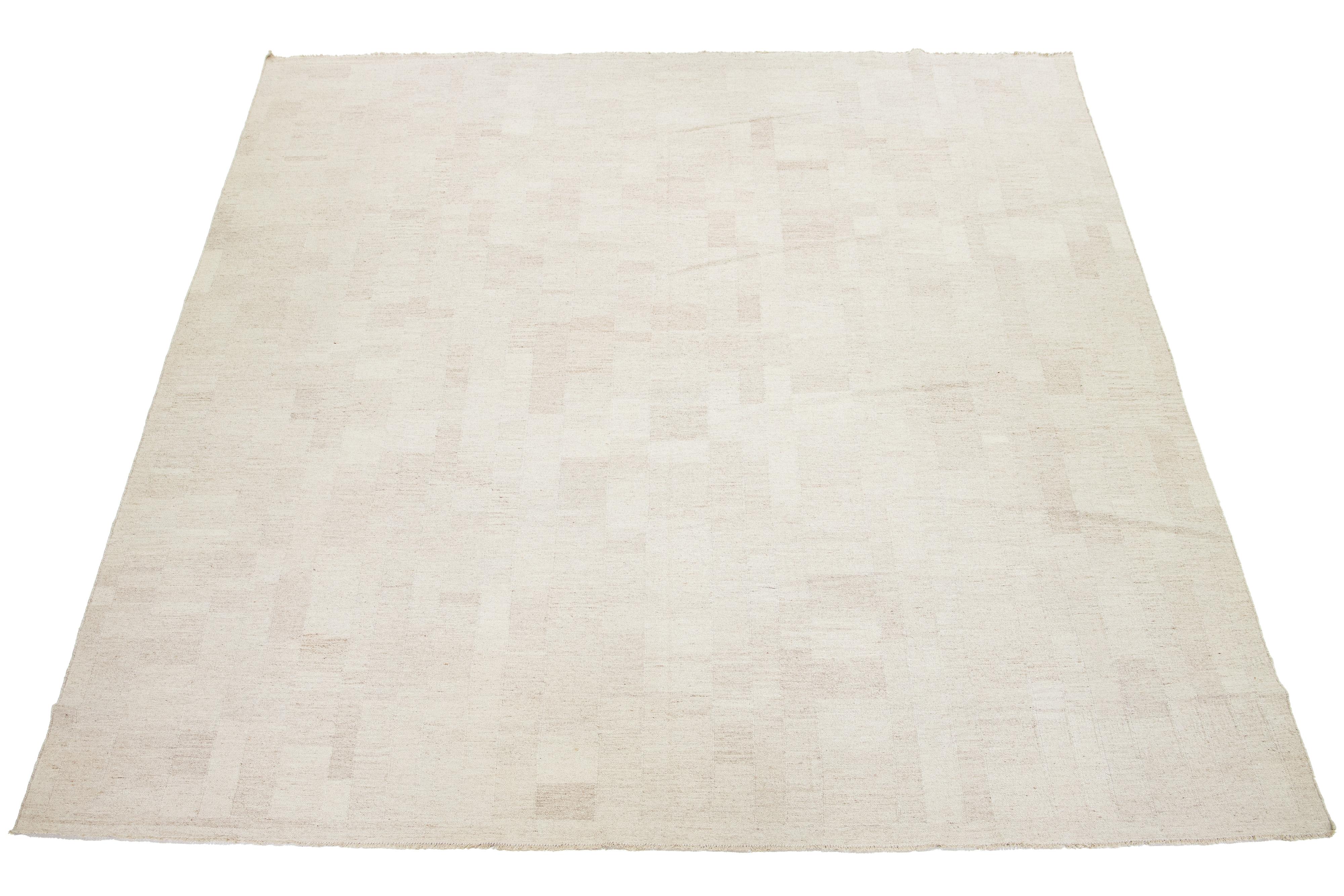 Ce tapis présente un splendide style contemporain Rug & Kilim à tissage plat, fabriqué à partir de laine de première qualité. Sa couleur beige dégage de l'élégance, complétée par un motif géométrique captivant qui se marie harmonieusement avec les