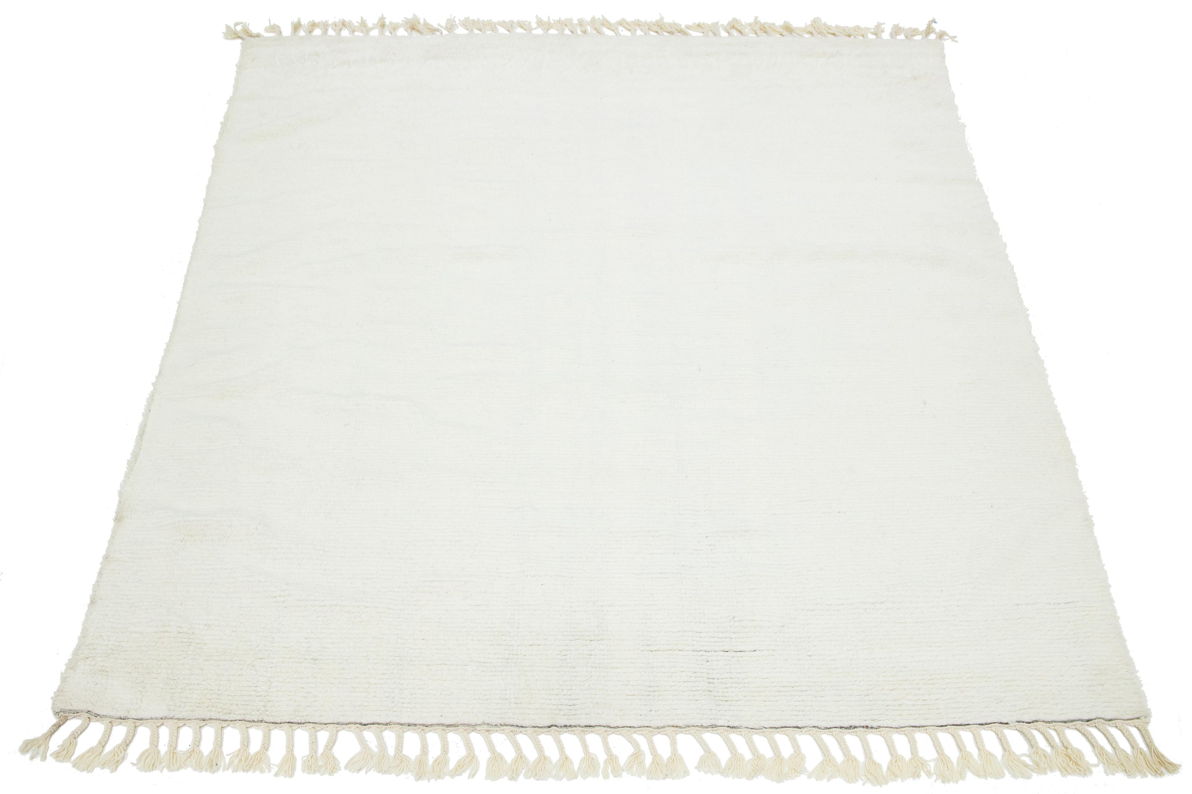 This contemporary Moroccan-style hand-knotted wool rug features an ivory field and fringes with a plush, solid design.

This rug measures 8' x 10'.

 