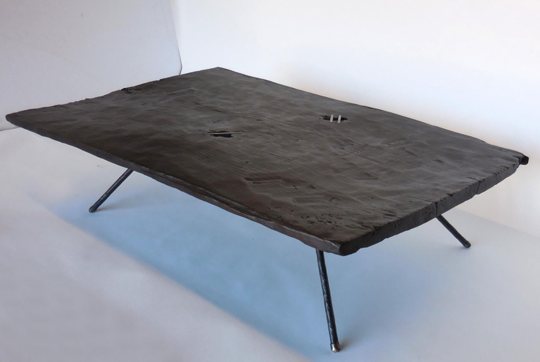 19th century one wide board in a dark brown, almost black patina atop four hand forged iron legs with bronze tips. Natural knots in wooden tops have been accented by three steel insets. The board is very old and hand hewn but smooth to the touch the