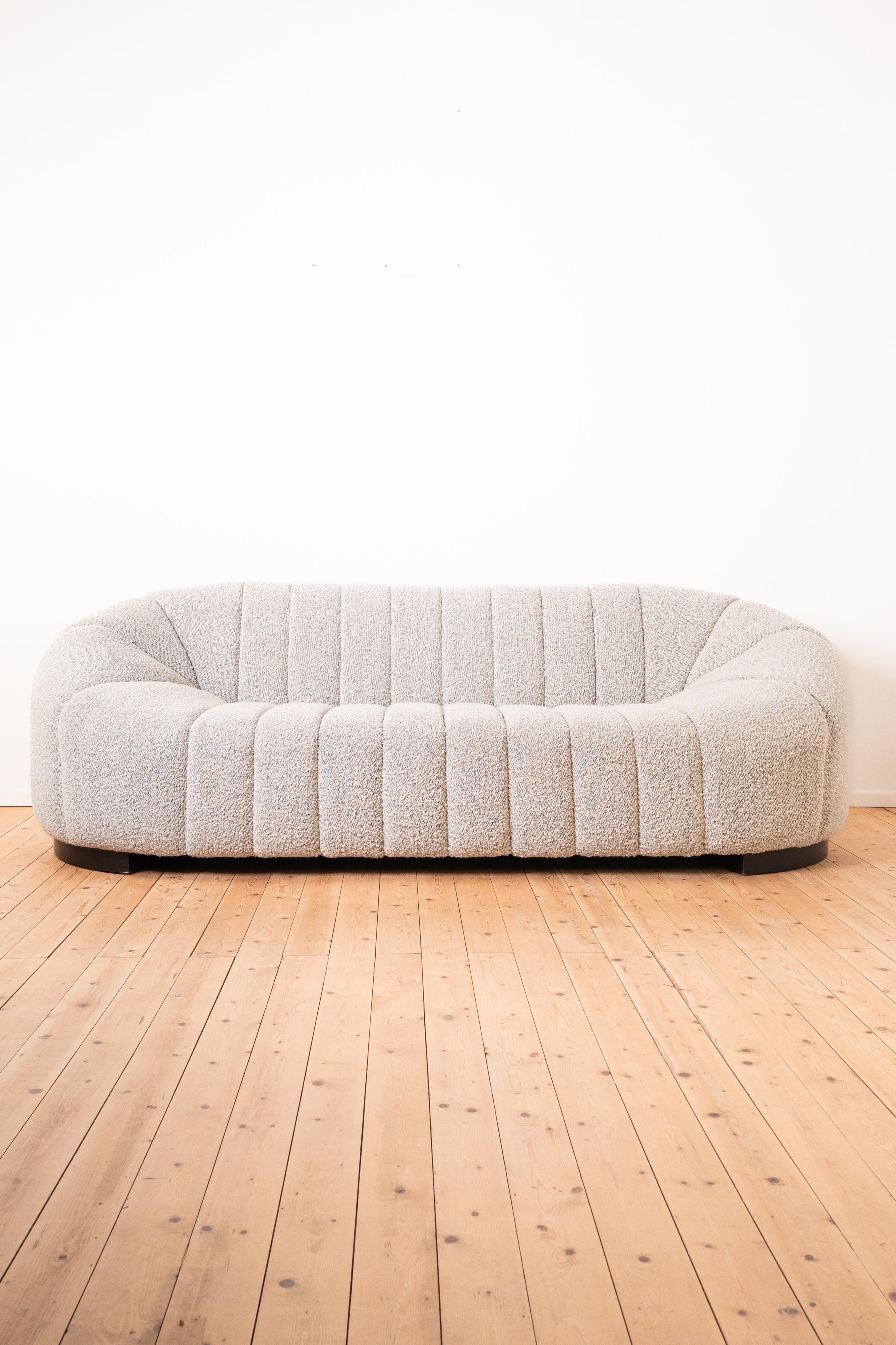 This sofa has a beautiful organic shape and even the wooden feet of the sofa are curb-shaped and follow the dimensions of the sofa. 

The sofa was upholstered with a soft, off-white bouclé fabric which gives the sofa a timeless appeal. 

This