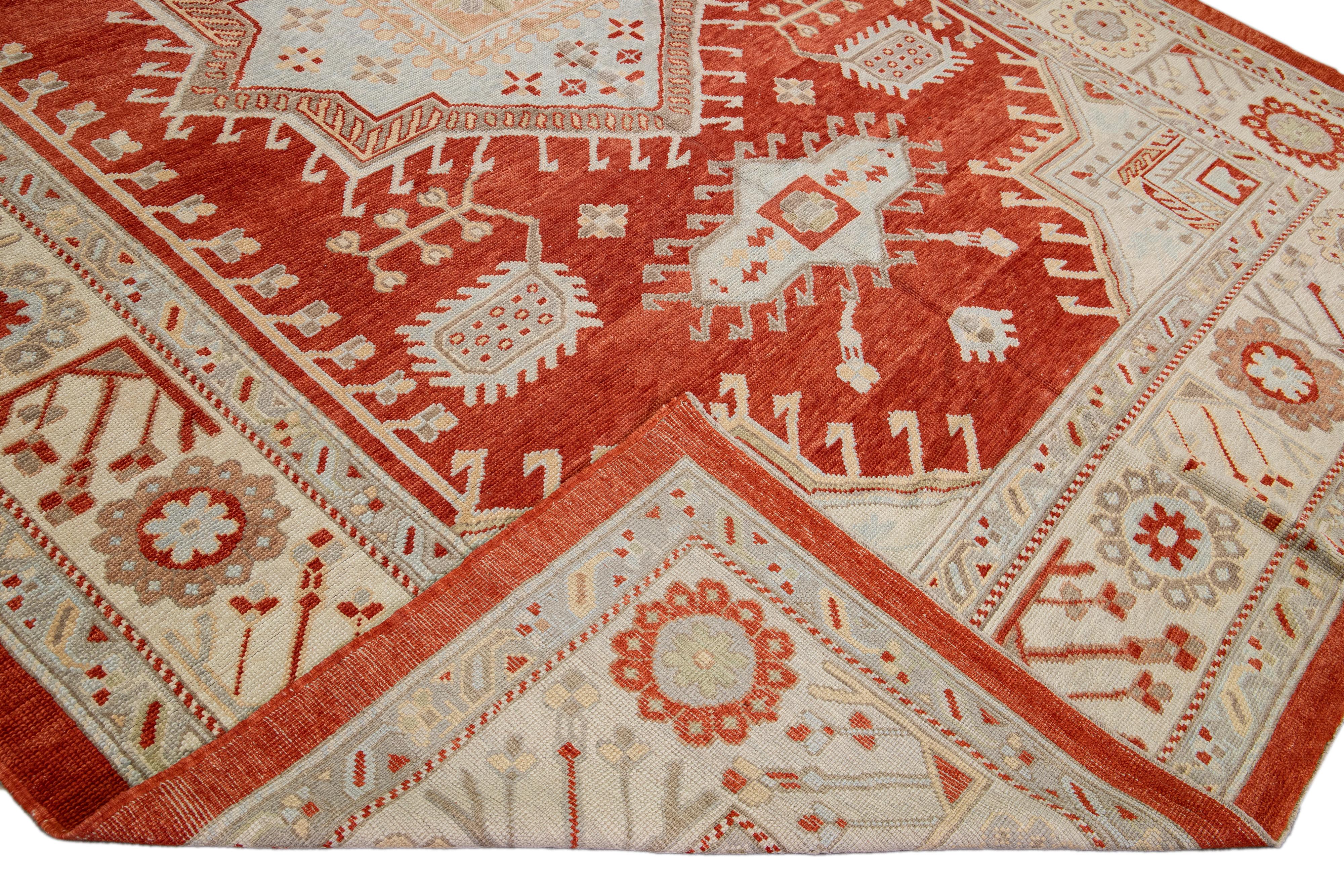 Schöner moderner, handgeknüpfter Oushak-Wollteppich mit einem terrakottafarbenen Feld. Dieses Stück hat einen beigefarbenen Rahmen, pfirsichfarbene und blaue Akzente, die ein wunderschönes geometrisches Medaillon-Design aufweisen.

Dieser Teppich