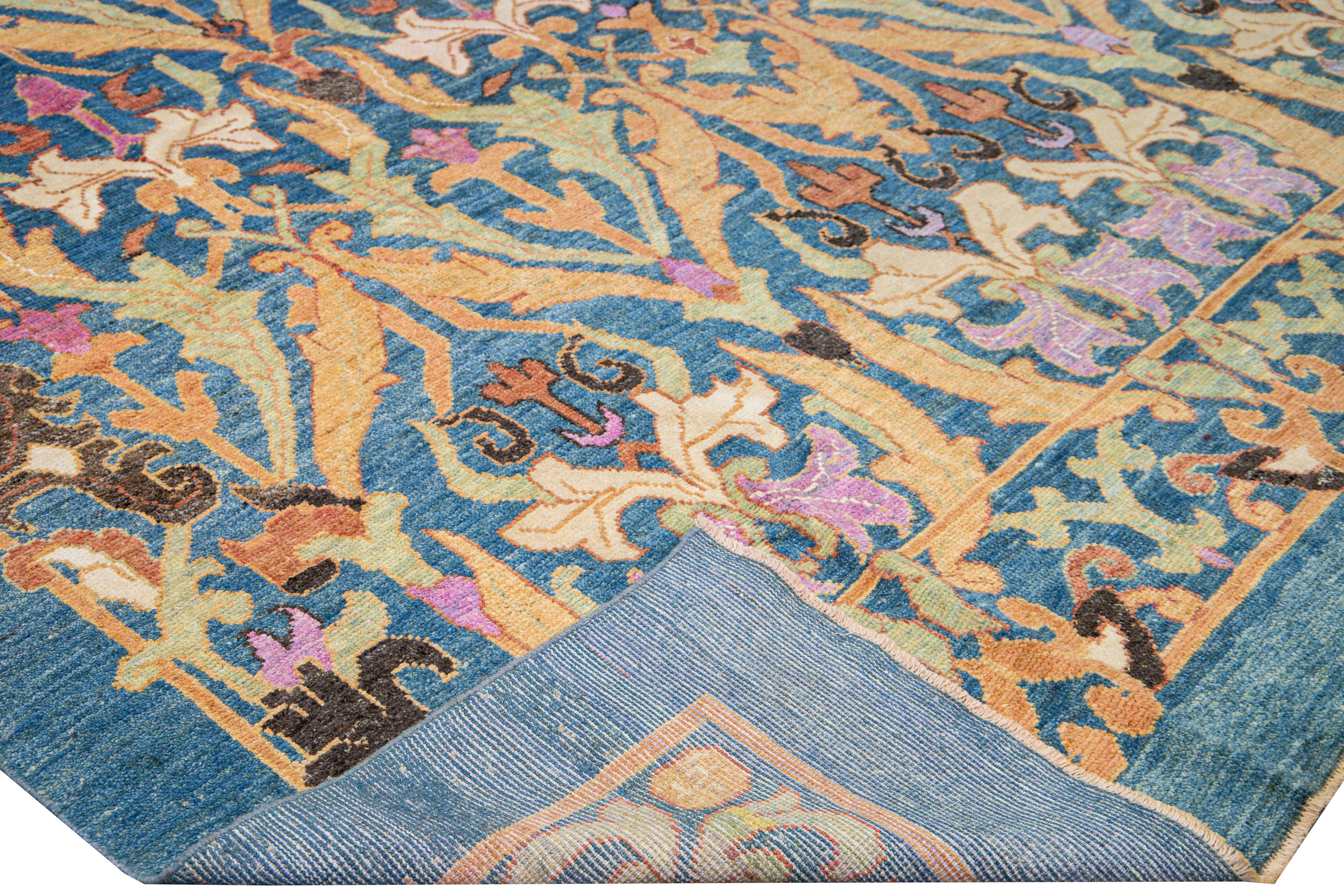 Beautiful modern Oushak hand-knotted wool rug with a blue field. This Oushak rug has orange, green, beige, pink, purple, and brown accents in a gorgeous floral pattern design. 

This rug measures: 13'9