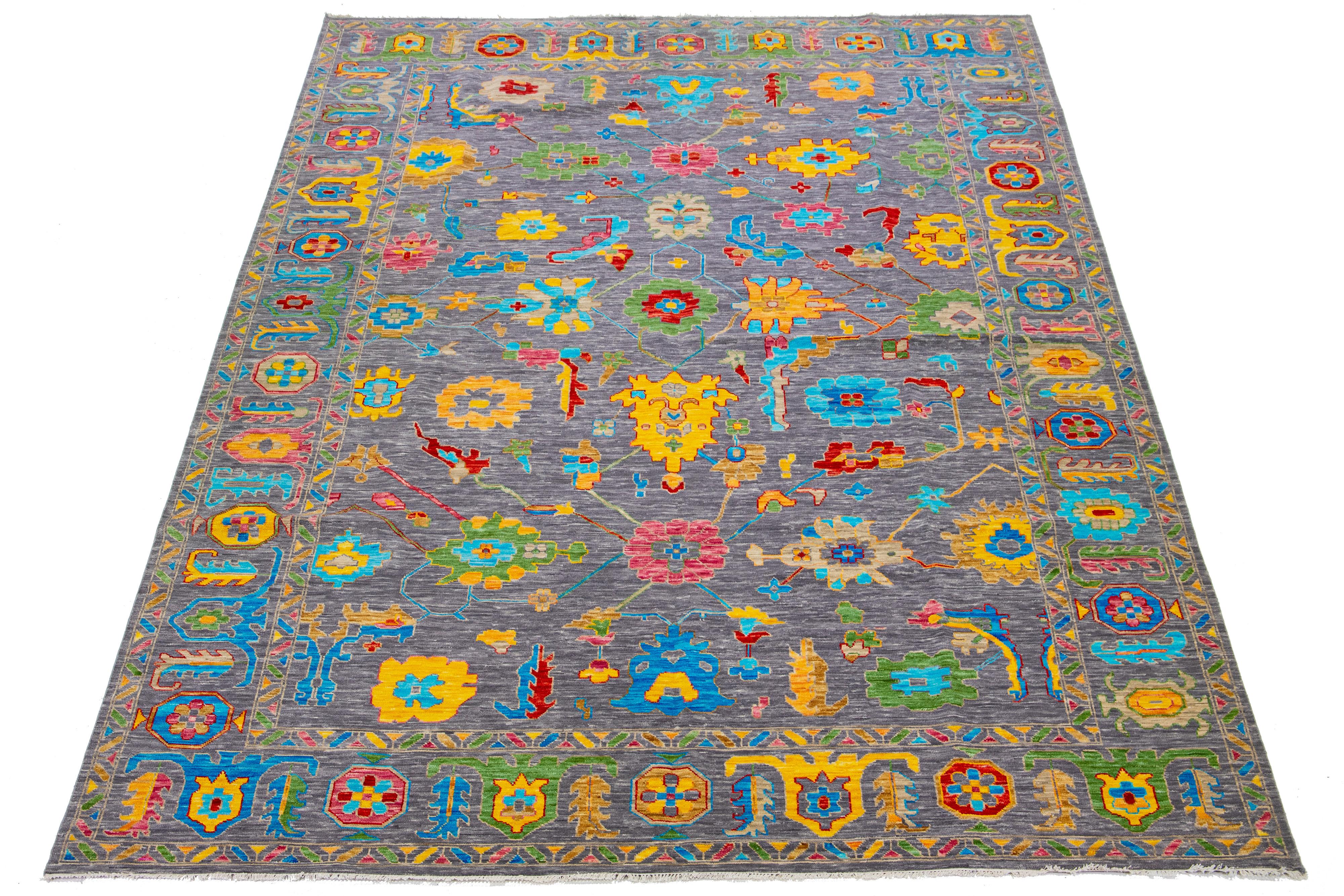This wool rug showcases a modern feel with its Oushak-style design. It features a hand-knotted gray field and is adorned with various vibrant floral patterns extending across the entire rug.

This rug measures 12'1